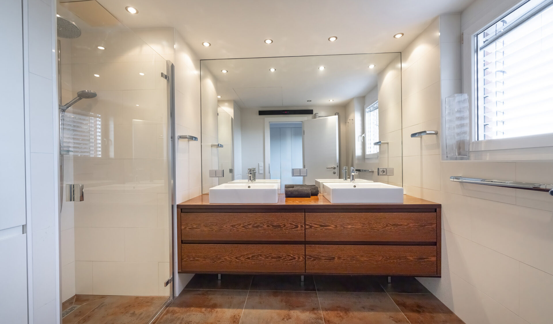 Badezimmer mit großem Spiegel, zwei Keramikwaschbecken und hölzernem Unterschrank.