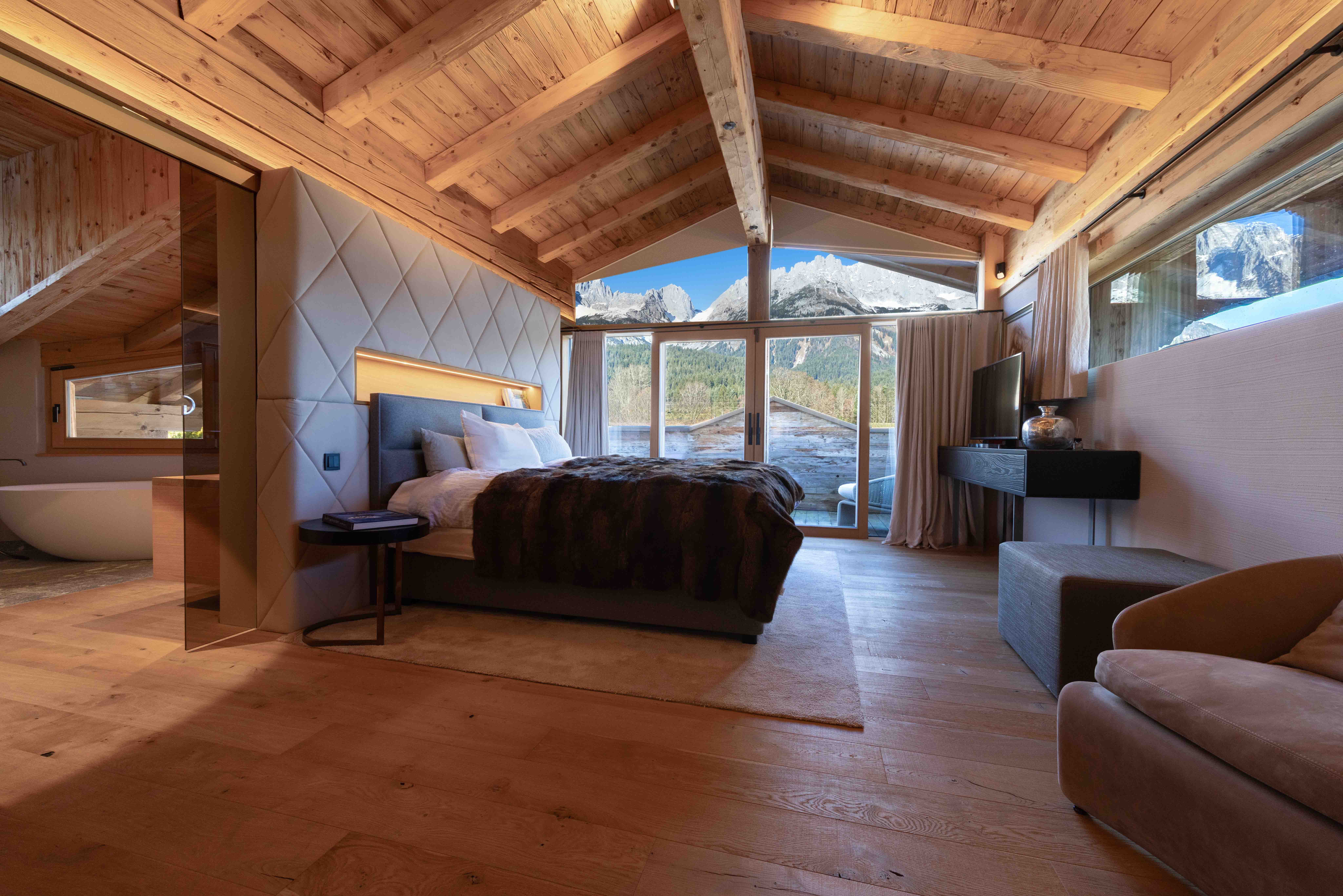 Luxuriöses Schlafzimmer eines Chalets mit offenem Badezimmer, Panoramafenstern und Bergblick.