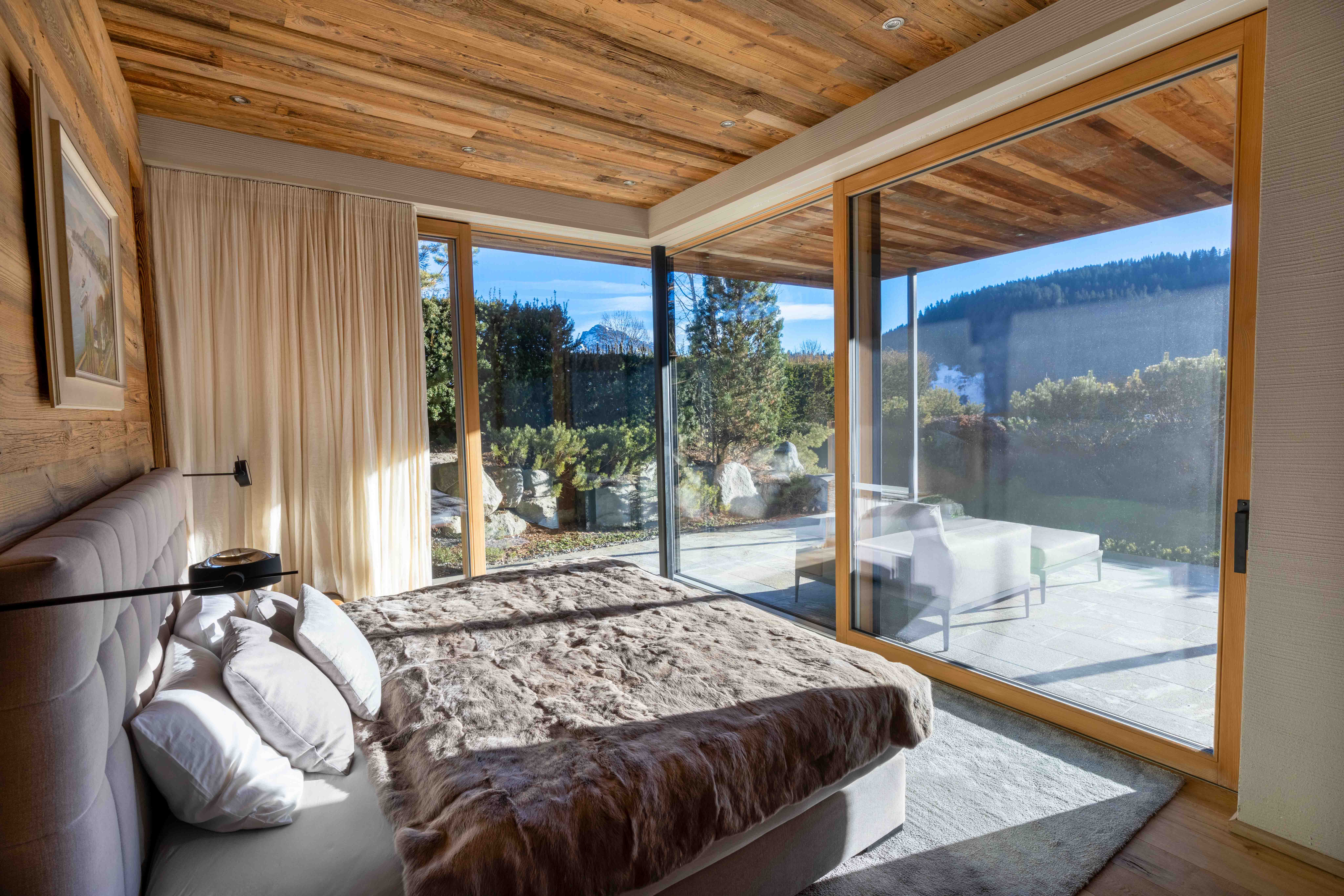 Helles Chalet-Schlafzimmer mit Eckfenstern, Terrasse und Panoramablick auf bewaldete Berge.