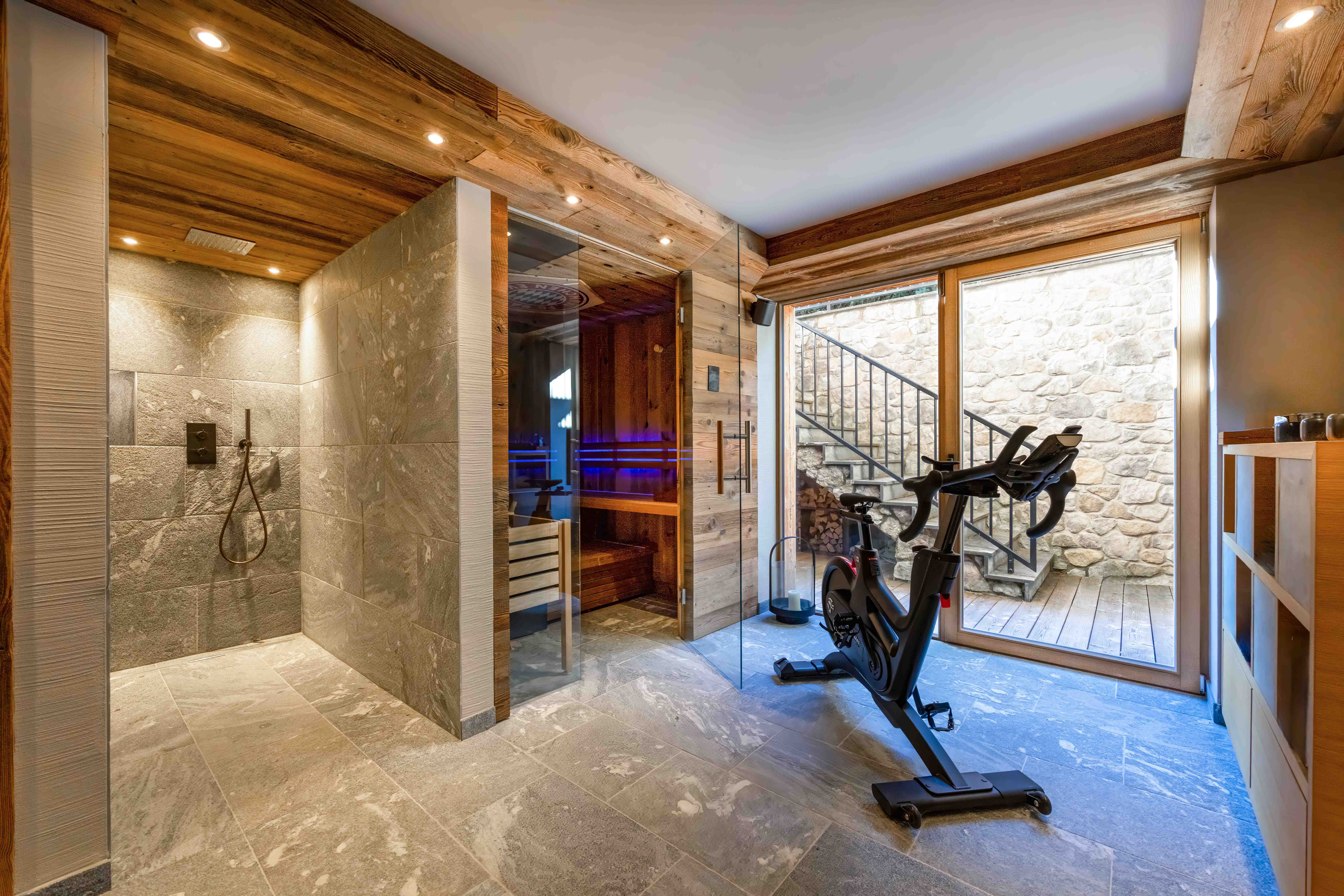 Wellness-Bereich eines Luxuslandhauses mit Sauna, Regendusche und Fitnessgeräten mit Außenzugang.