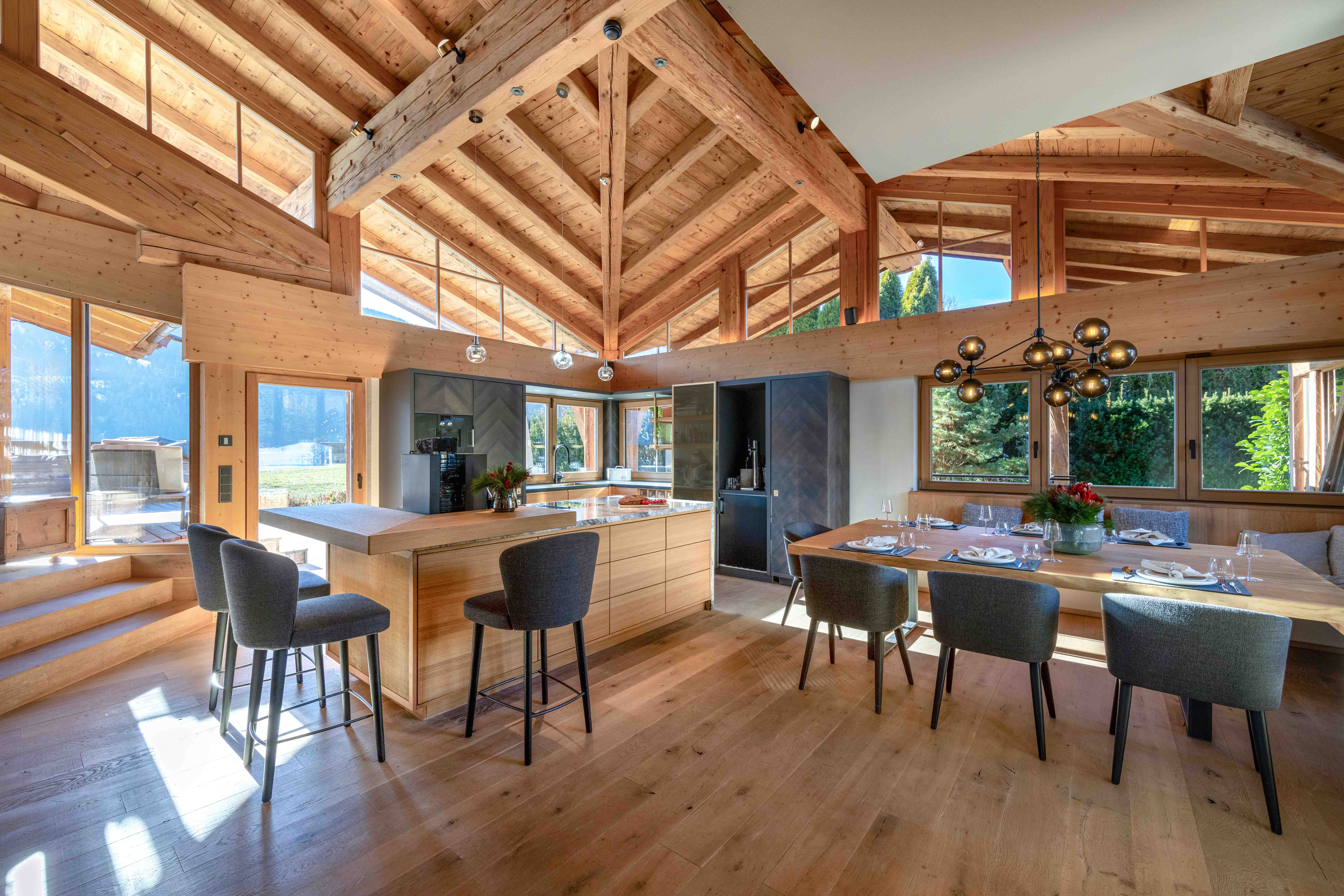 Offene Wohnküche eines Luxus-Chalets mit Kochinsel, Essbereich und hoher Holzdecke.