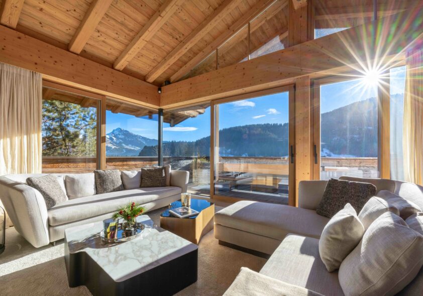 Luxuriöses Landhauswohnzimmer mit Holzdecke, beigem Sofa und Panoramablick auf Berge.