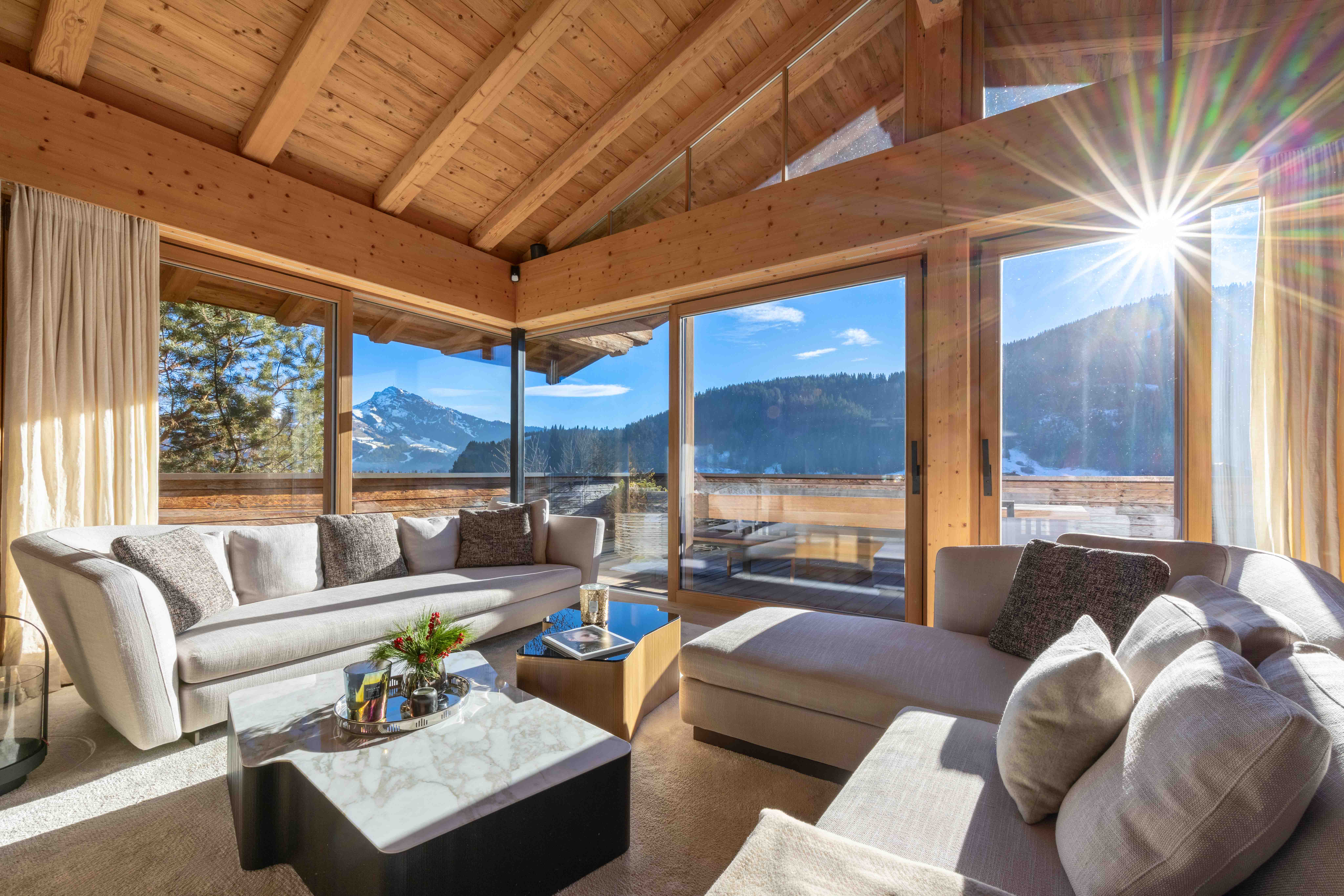 Luxuriöses Landhauswohnzimmer mit Holzdecke, beigem Sofa und Panoramablick auf Berge.