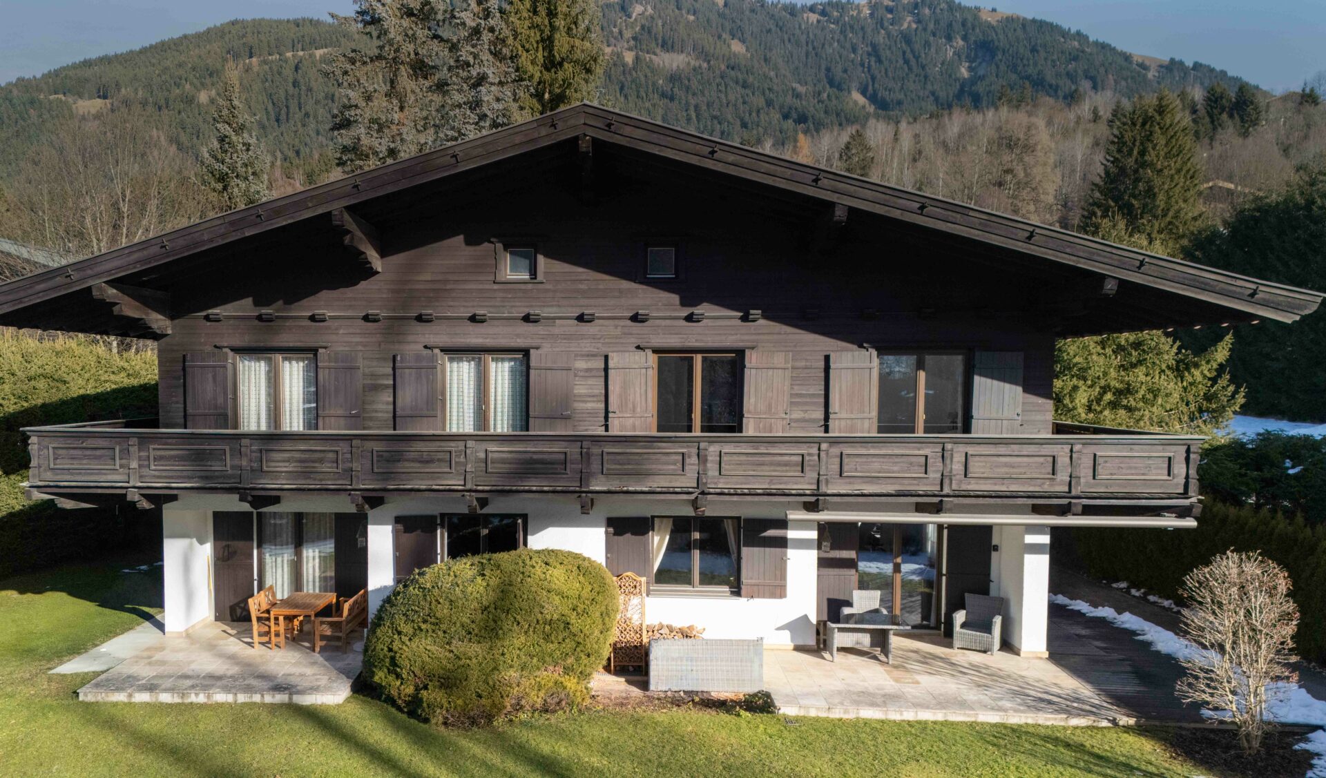 Traditionelle Doppelhaushälfte mit dunkler Holzfassade, Terrasse und Bergblick.