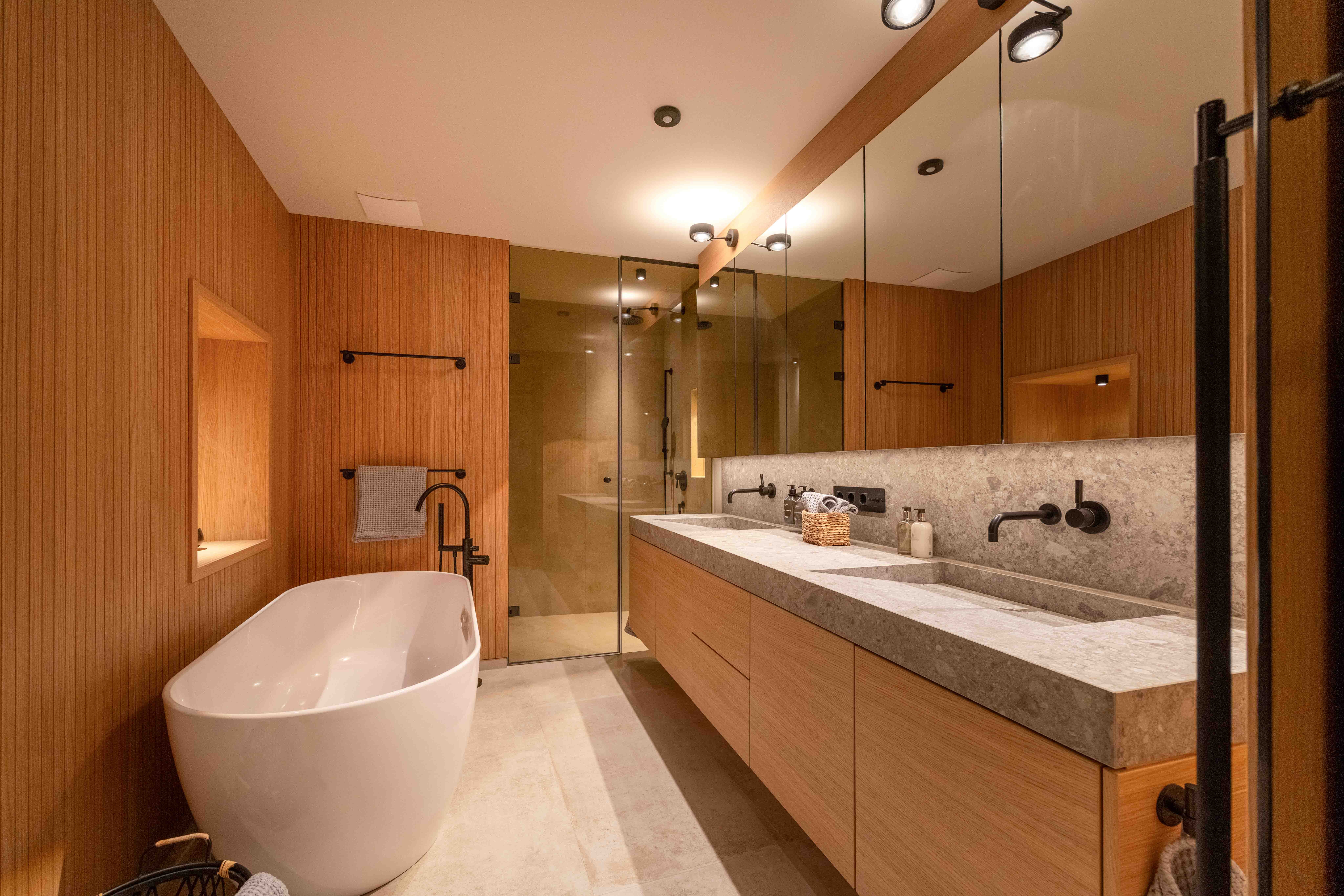 Luxus-Badezimmer mit gerillter Holzvertäfelung, freistehender Wanne und Stein-Doppelwaschtisch.