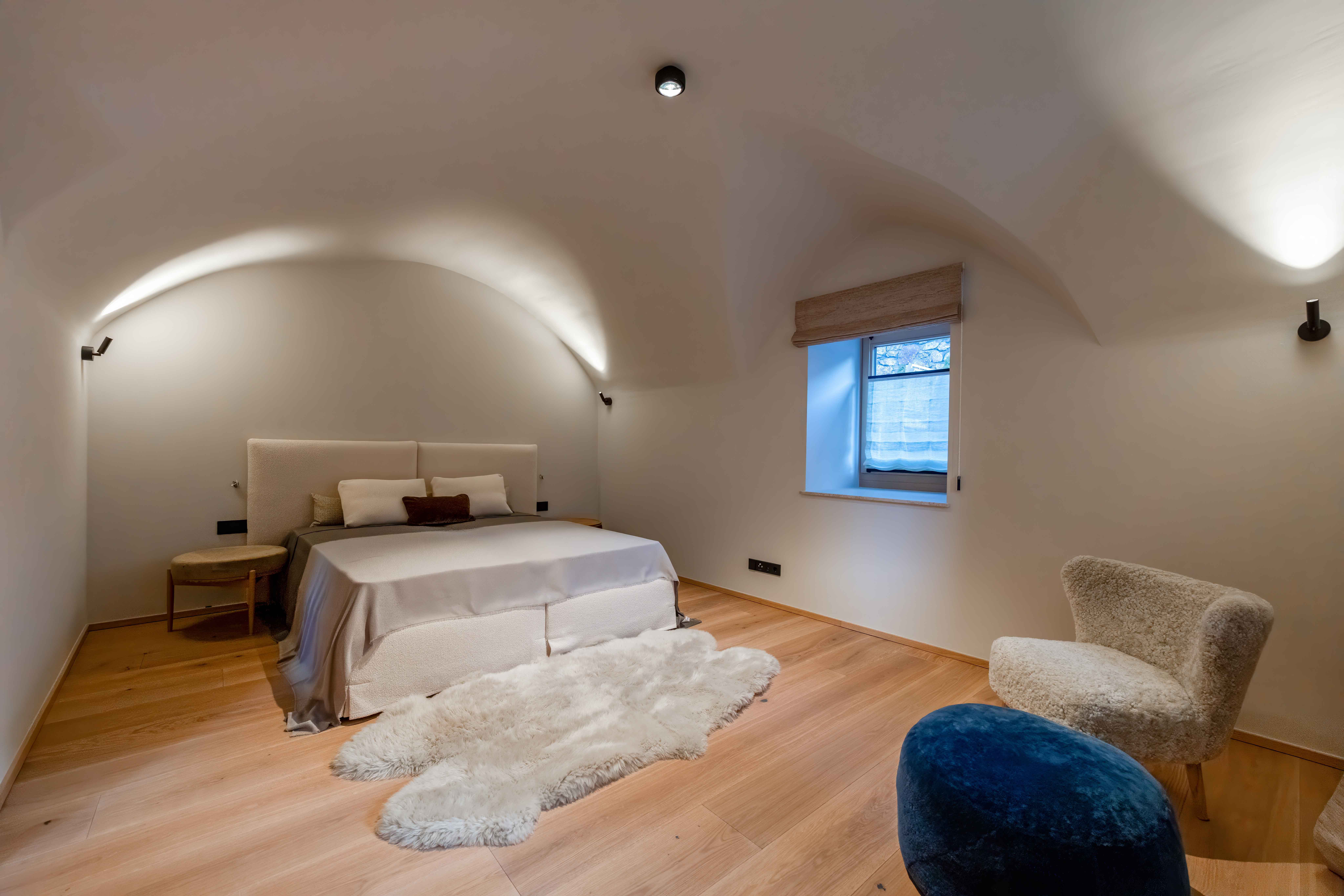 Minimalistisches Schlafzimmer mit gewölbter Bogendecke, Doppelbett und Designer-Sessel.