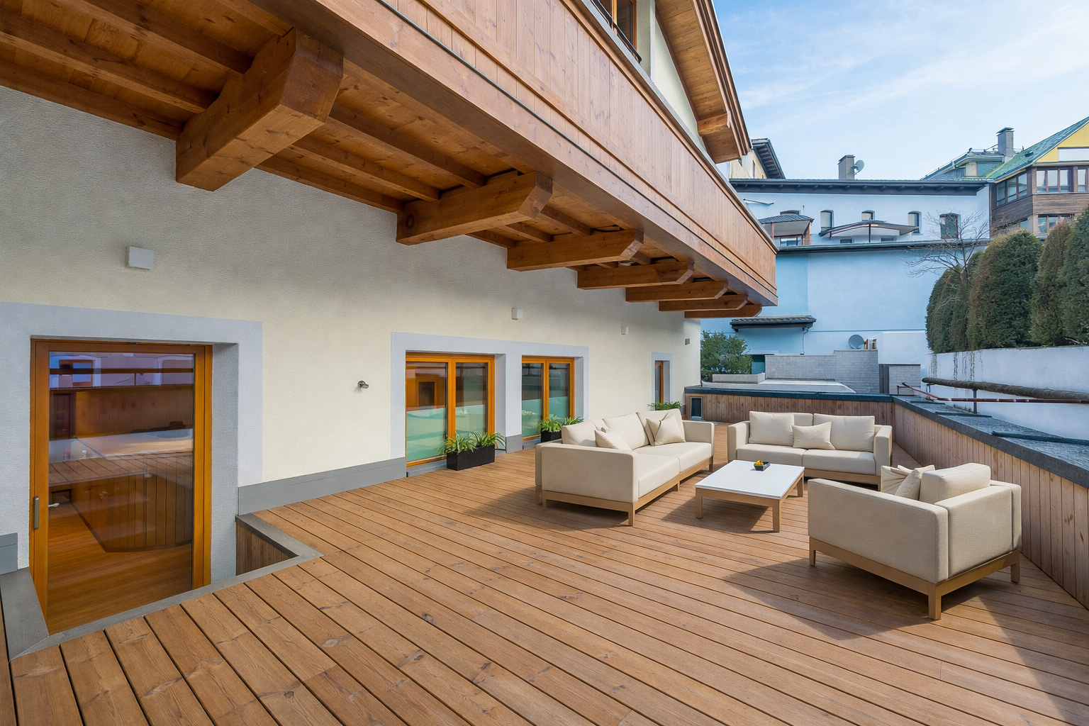 Moderne Apartment-Dachterrasse mit Holzdeck, Lounge-Möbeln und Blick auf Stadtlandschaft.