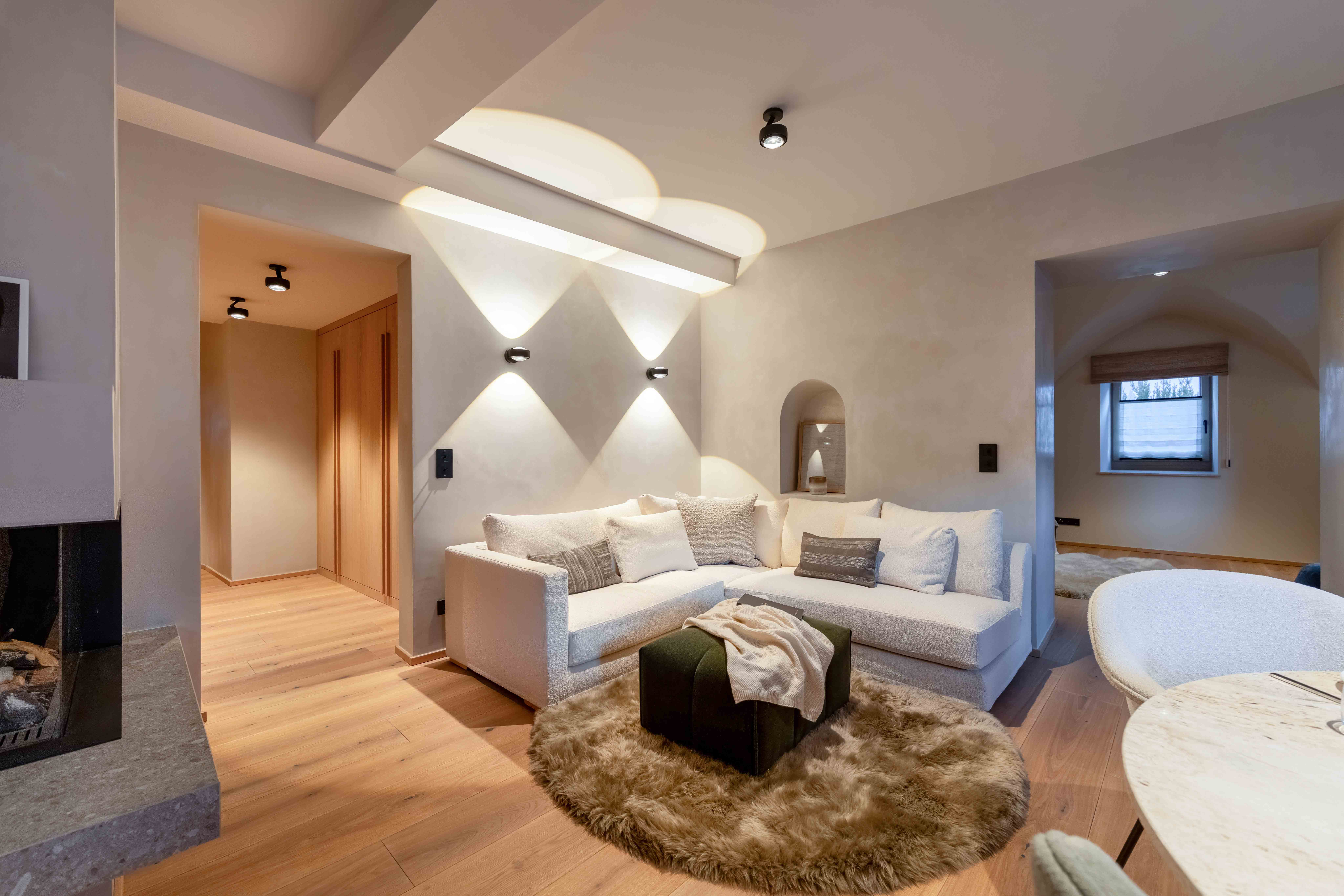 Modernes Wohnzimmer mit skulpturaler Wandbeleuchtung, weißem Ecksofa und Rundbogen-Architektur.