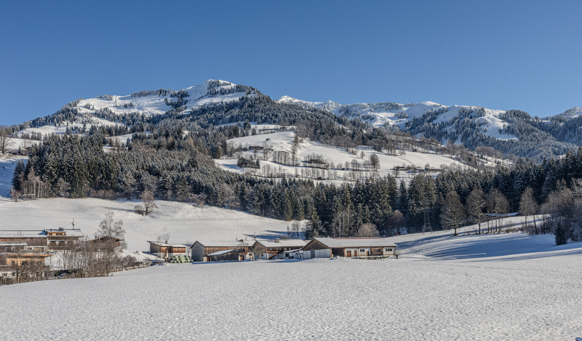 Panoramablick auf verschneite Alpenlandschaft mit Berggipfeln und Chalets.