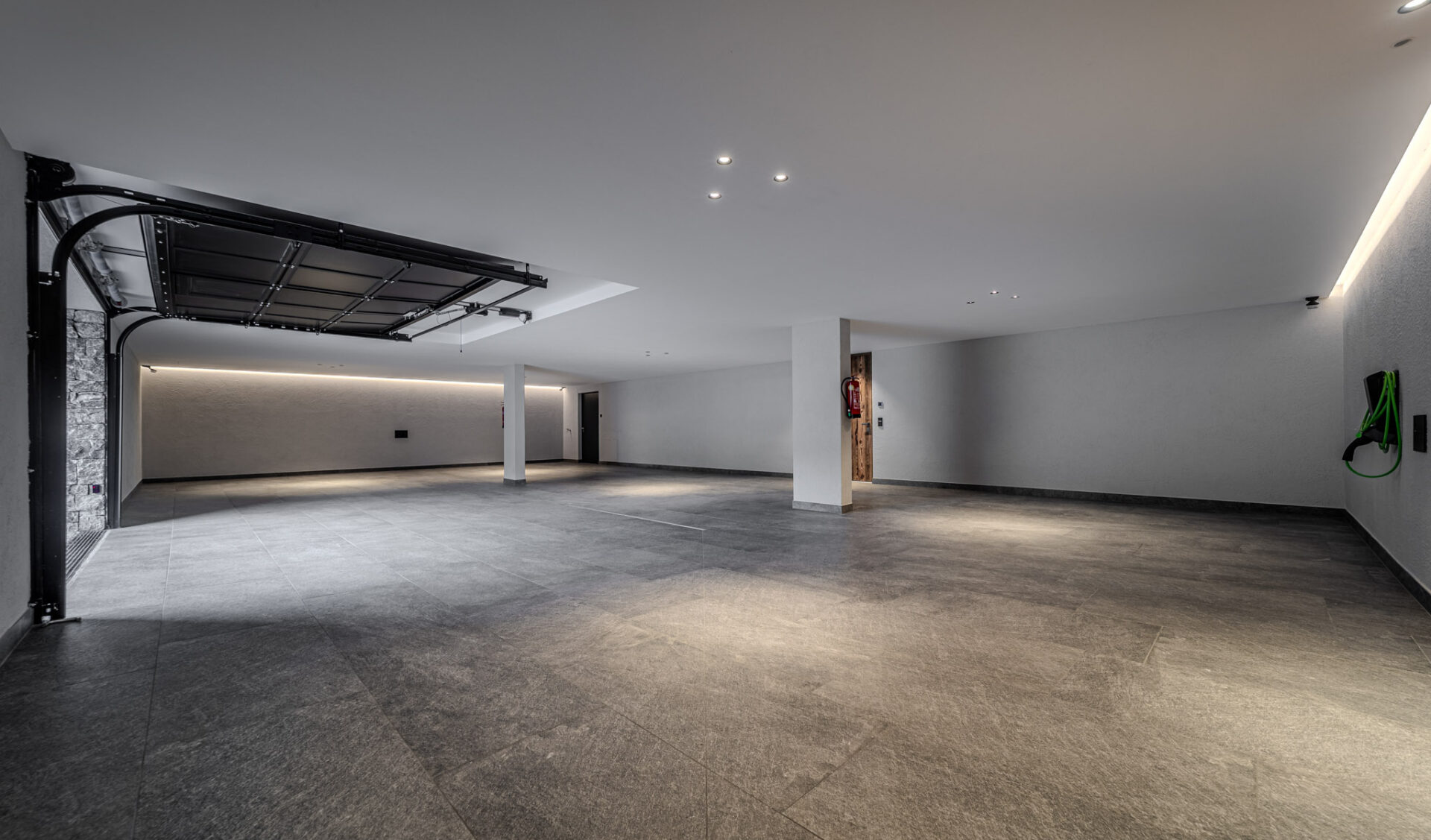 Geräumige Tiefgarage mit E-Ladestation, Wandbeleuchtung und dunklem Fliesenboden.