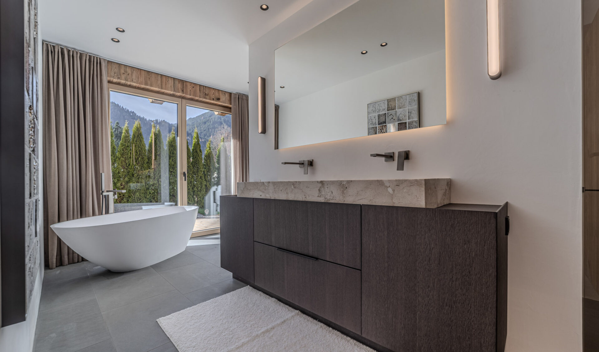 Lichtdurchflutetes Badezimmer mit freistehender Badewanne und Bergblick.