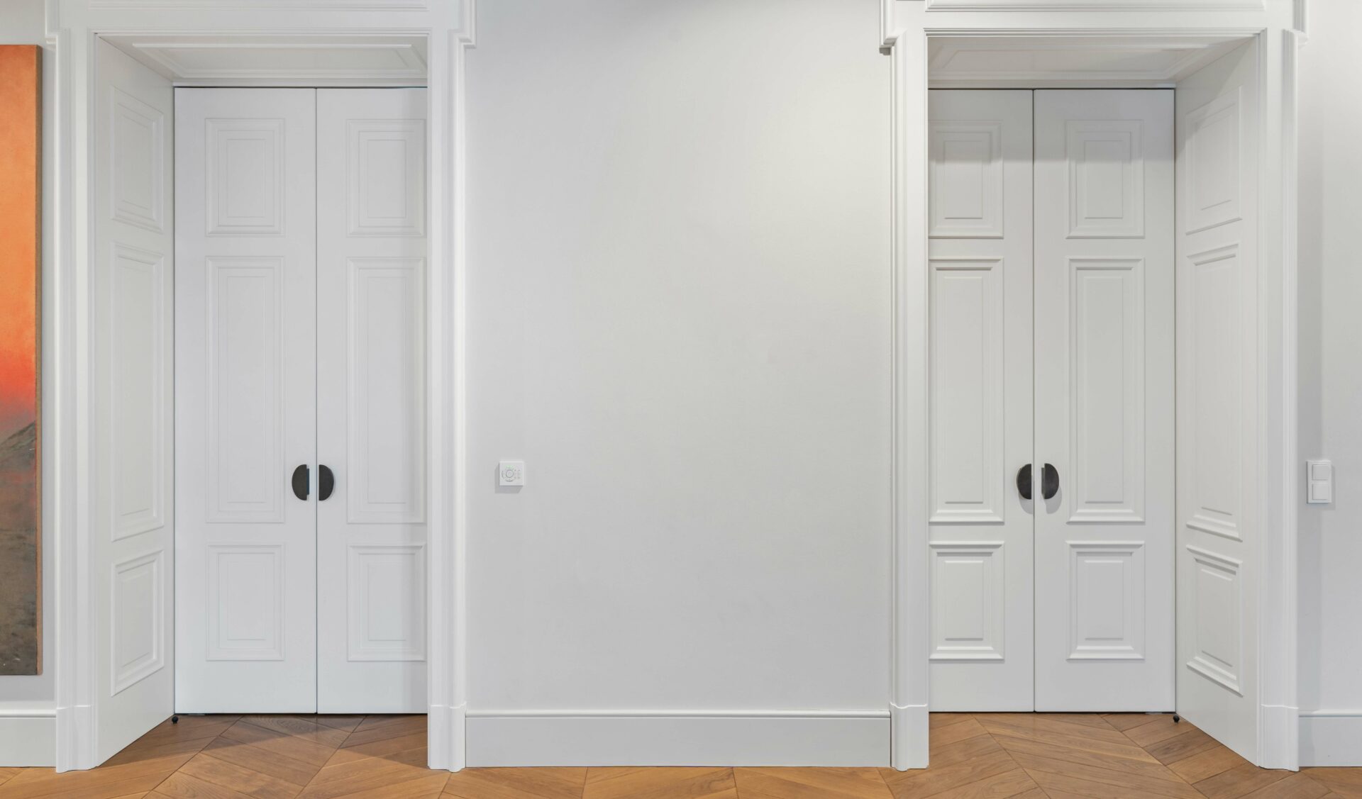 Symmetrischer Altbau-Flur mit weißen Doppelflügeltüren, Fischgrätparkett und hohen Decken.