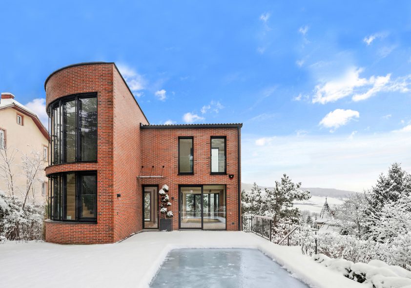 Moderne Neubau-Villa mit rundem Turmelement und Panoramaterrasse in Hanglage mit Winterblick.