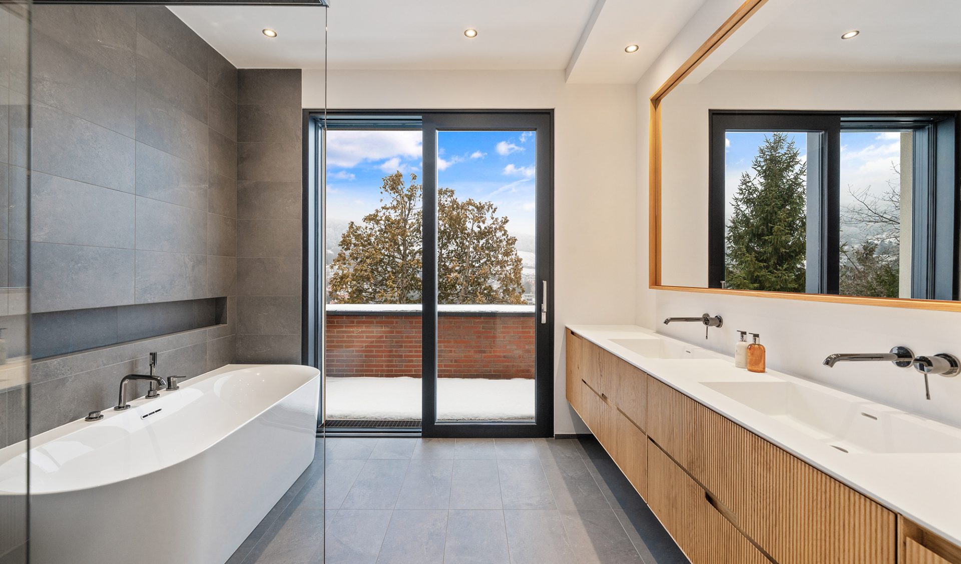 Modernes En-suite-Badezimmer mit weißer Badewanne, Doppelwaschtisch und Terrassenzugang.