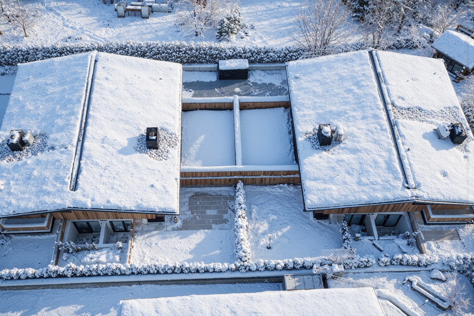 Luftbild moderner Holzchalets mit Flachdach und separaten Gärten in verschneiter Berglandschaft.