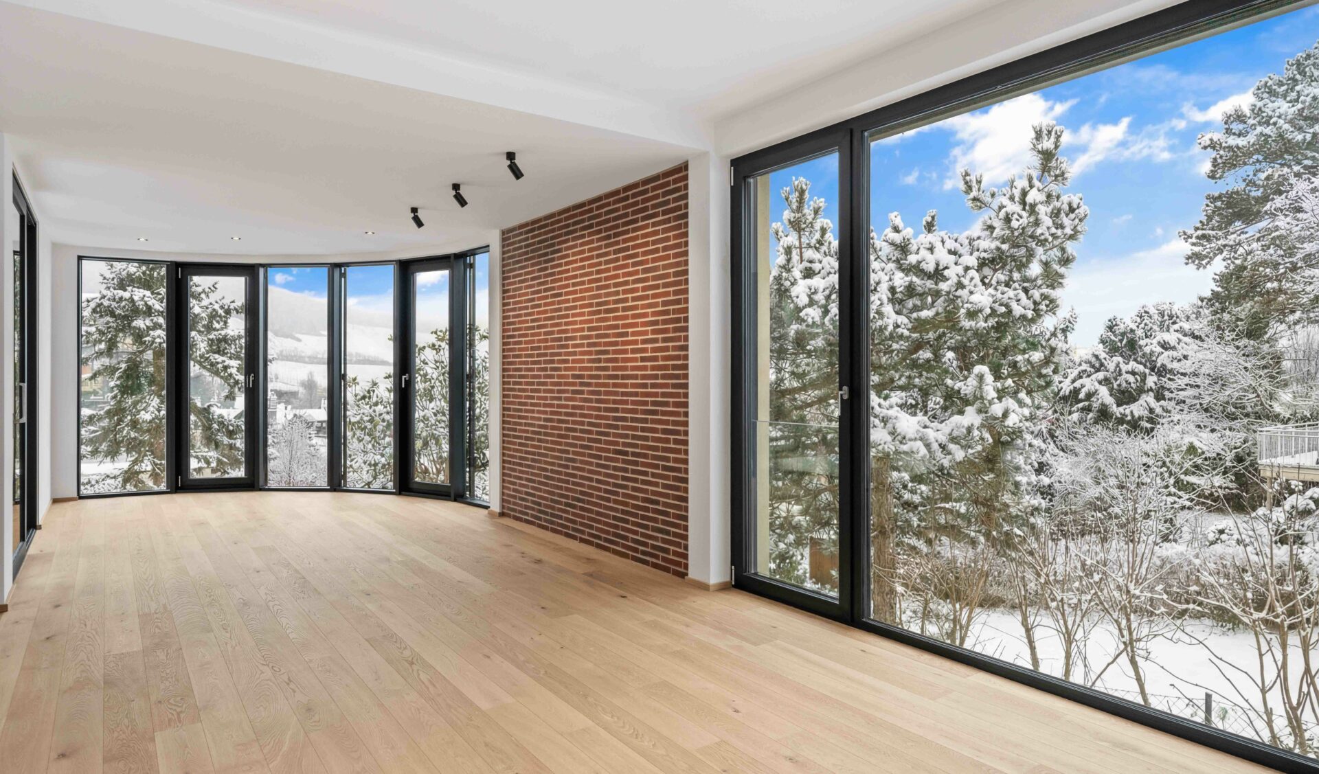 Loftartiger Wohnraum mit geschwungener Panoramaverglasung, Sichtmauerwerk und Naturblick.