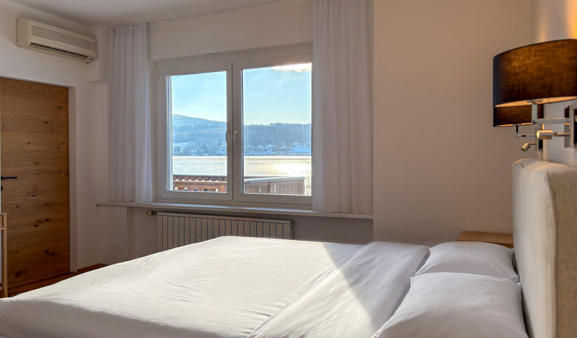 Helles Schlafzimmer mit Seeblick und Doppelbett. Modernes Zimmer mit Klimaanlage und großen Fenstern.