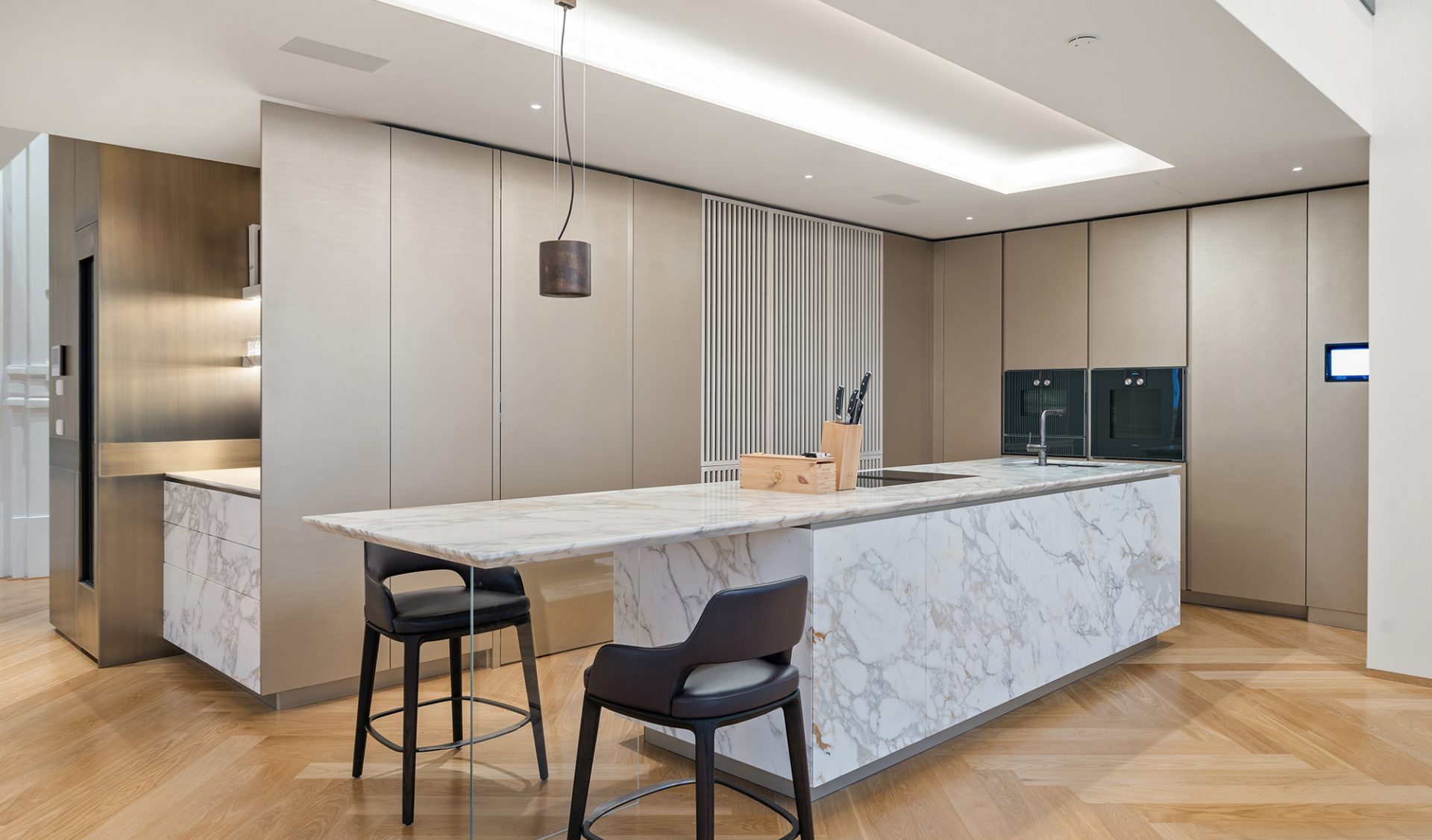 Premium-Einbauküche mit Marmor-Kücheninsel, integrierten Geräten, Pendelleuchte und Fischgrätparkett.