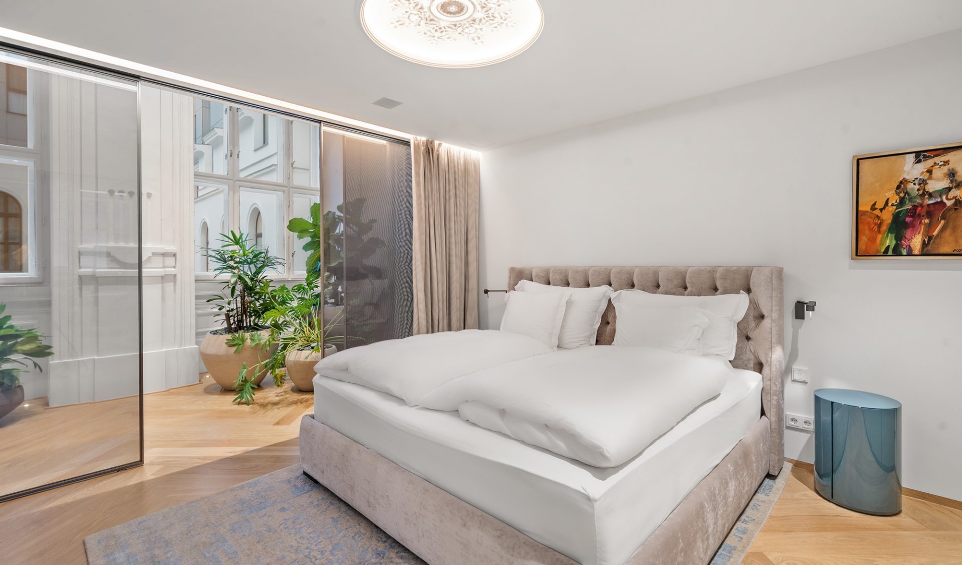 Zurückgezogenes En-suite-Schlafzimmer mit Glastrennwand, üppiger Bepflanzung und Fischgrätparkett.