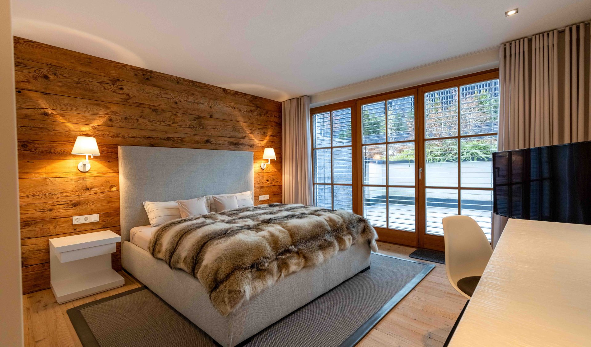 Master-Bedroom mit Altholz-Kopfteil, Wandleuchten, Arbeitsplatz und direktem Balkonzugang.