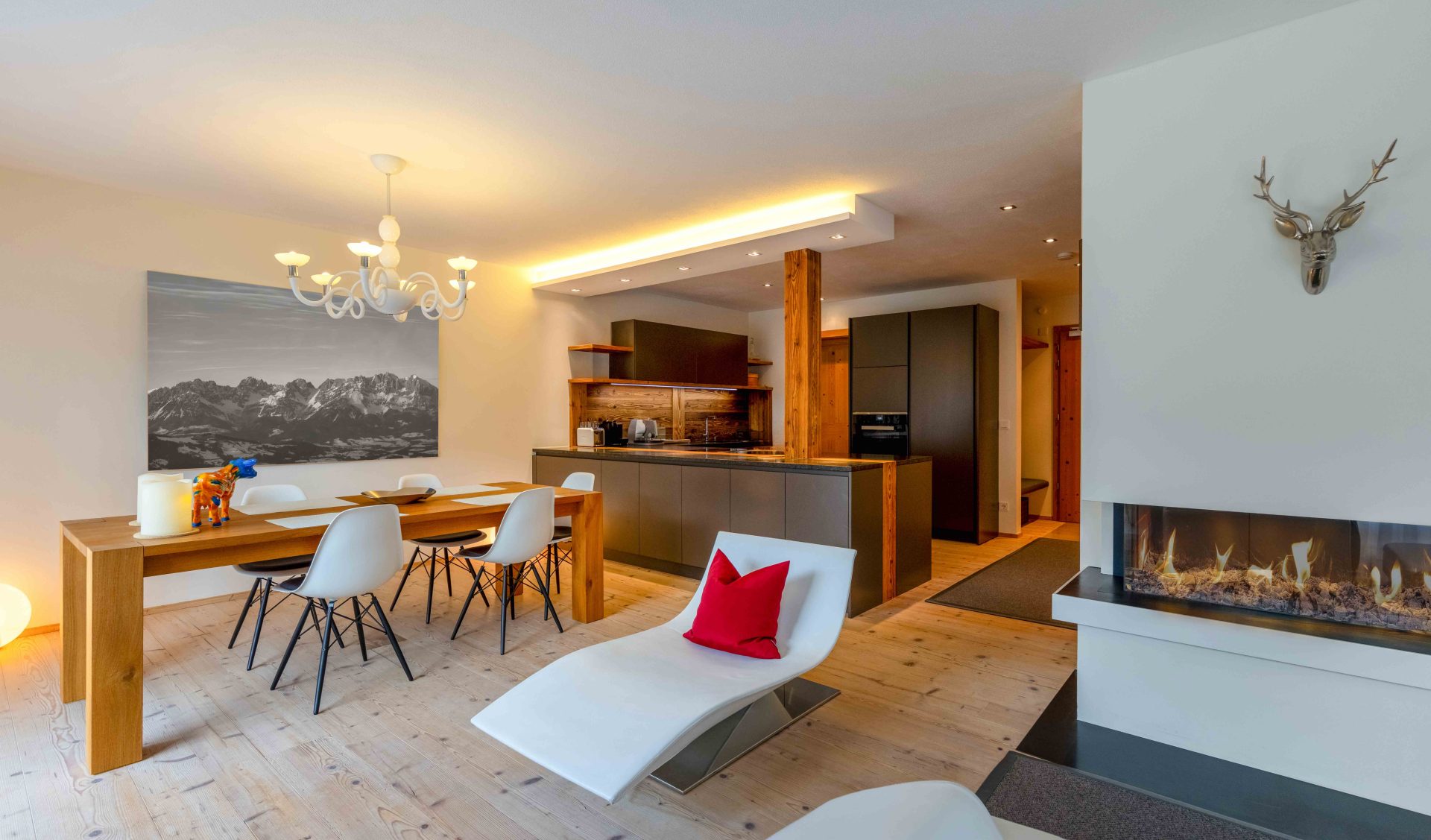 Moderner Wohn-Essbereich mit Designer-Küche, Panoramakamin, Holztisch und alpinem Bergbild-Akzent.