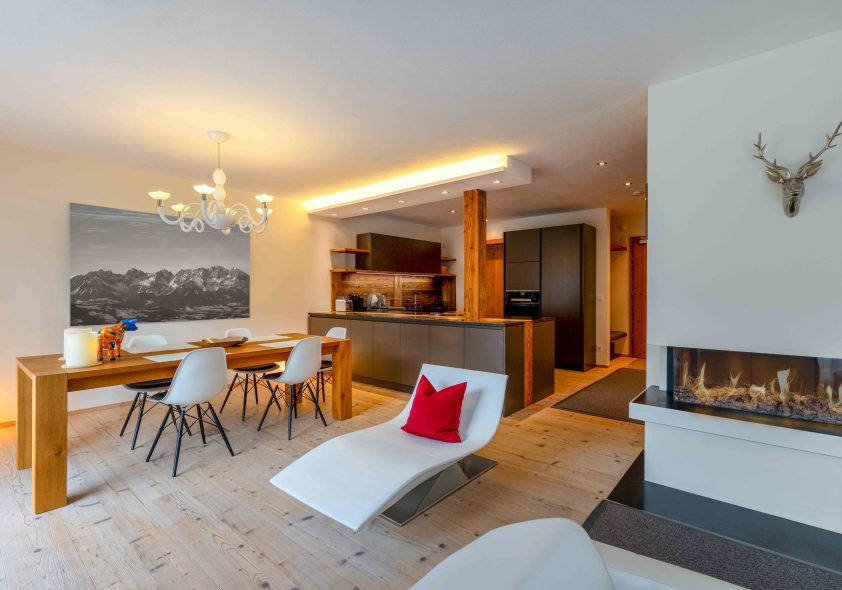 Moderner Wohn-Essbereich mit Designer-Küche, Panoramakamin, Holztisch und alpinem Bergbild-Akzent.