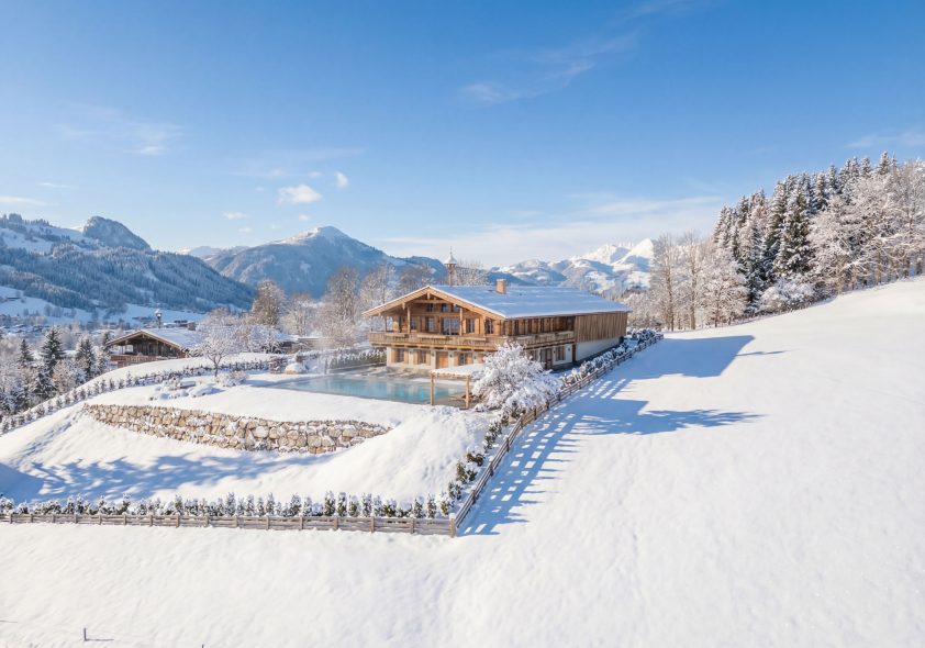 Visualisierung eines verschneiten Luxus-Chalets mit dampfenden Outdoor-Pool vor majestätischer Bergkulisse im Sonnenlicht.