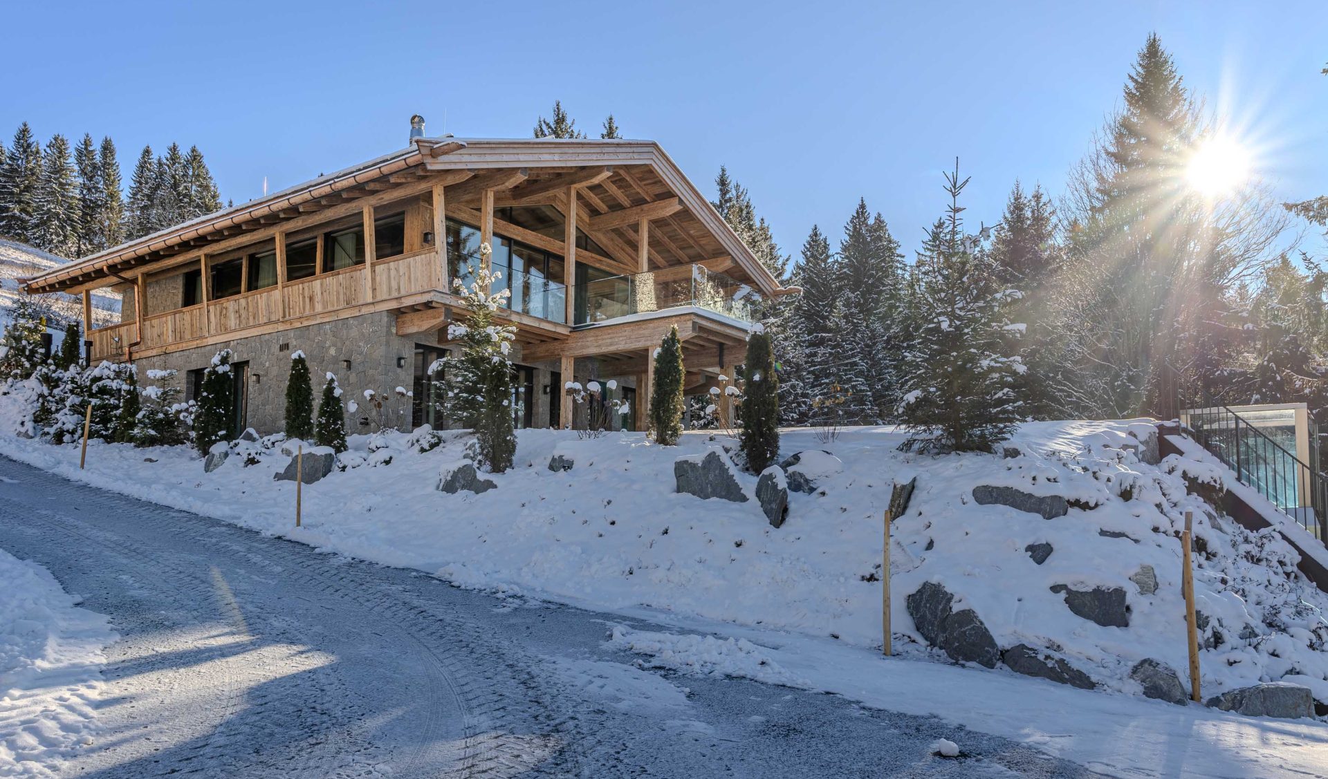 Exklusives Alpen-Chalet mit Natursteinsockel, Holzbalkon und verschneitem Vorgarten im Wintersonnenglanz.