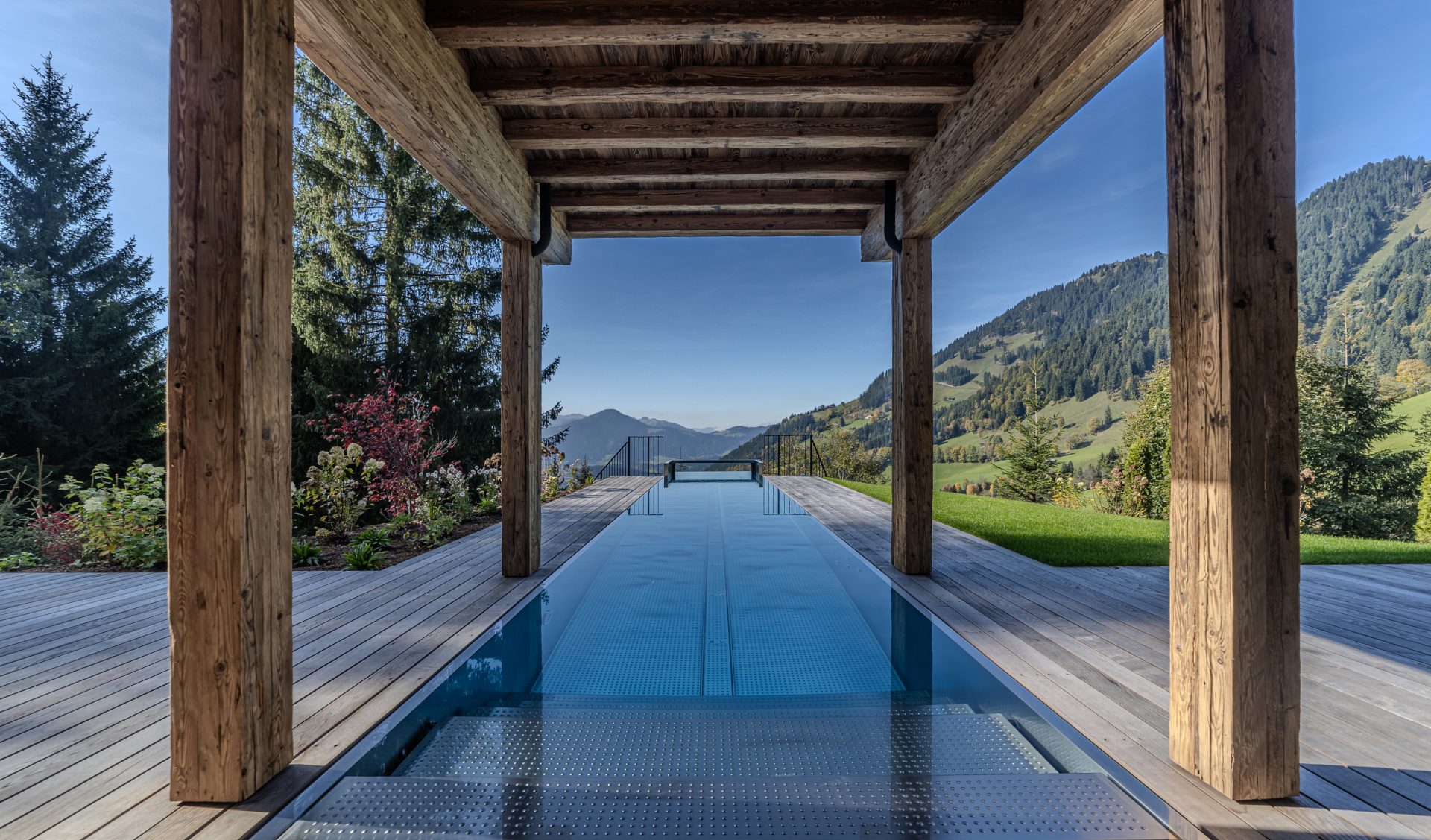 Luxus-Infinity-Pool mit Altholz-Pergola und spektakulärem Alpenpanorama auf Holzdeck-Terrasse.