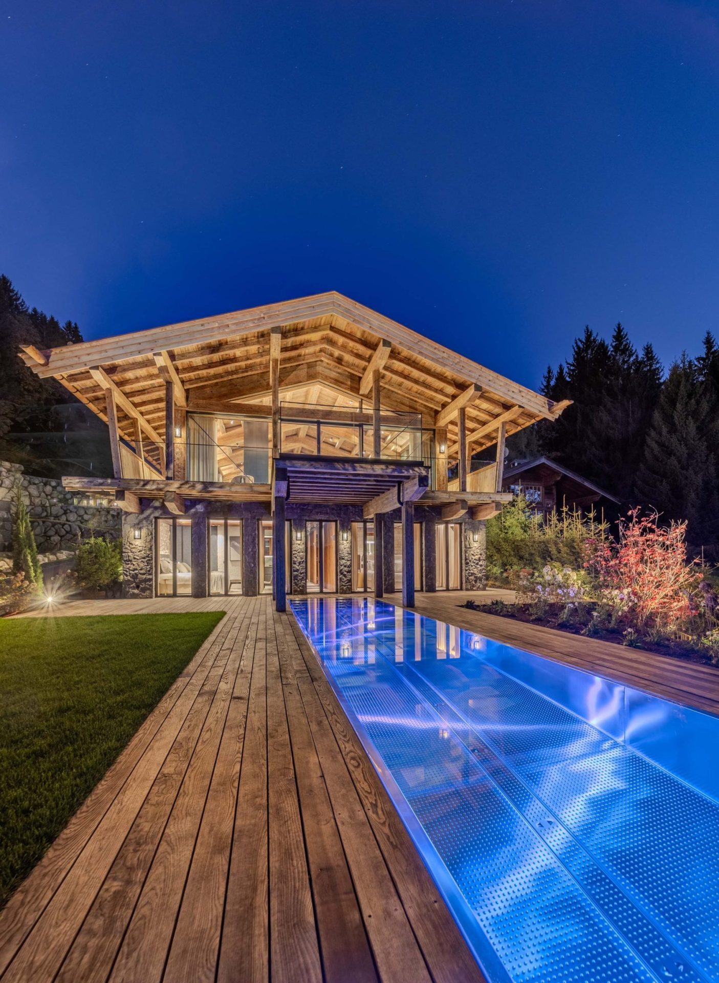 Premium-Bergchalet mit Infinity-Pool, LED-Beleuchtung, Naturstein und Panoramaverglasung bei Abendlicht.