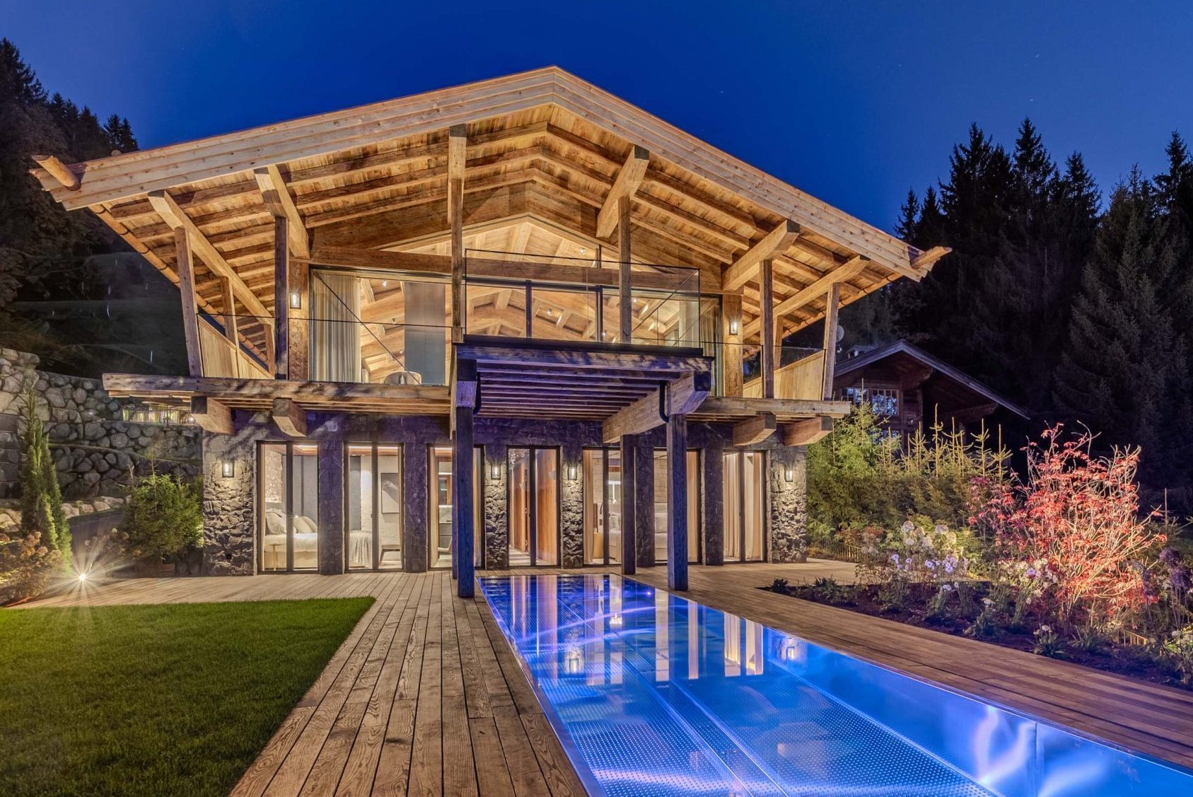 Premium-Bergchalet mit Infinity-Pool, LED-Beleuchtung, Naturstein und Panoramaverglasung bei Abendlicht.