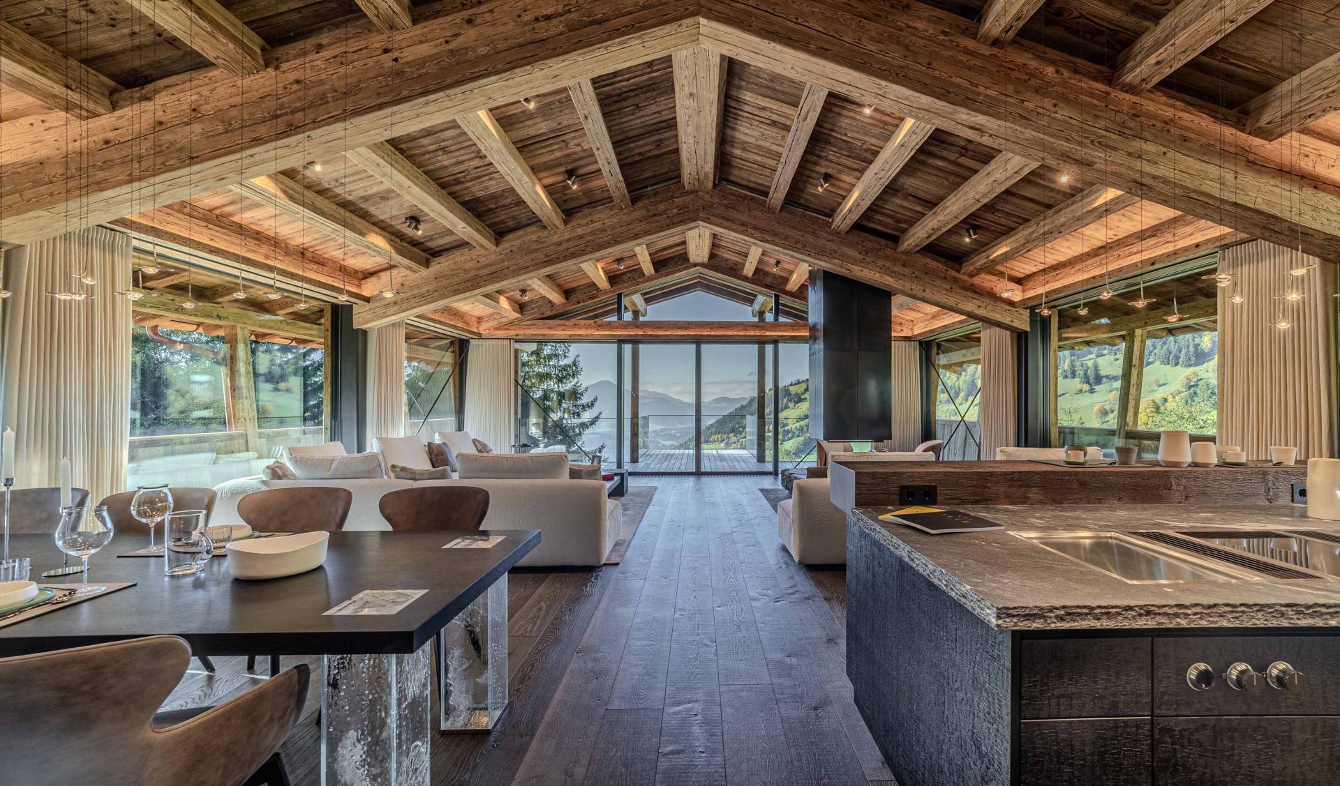 Weitläufiger offener Wohnbereich mit Altholz-Dachstuhl, Designer-Küche, Kaminofen und Panoramablick auf Alpen.