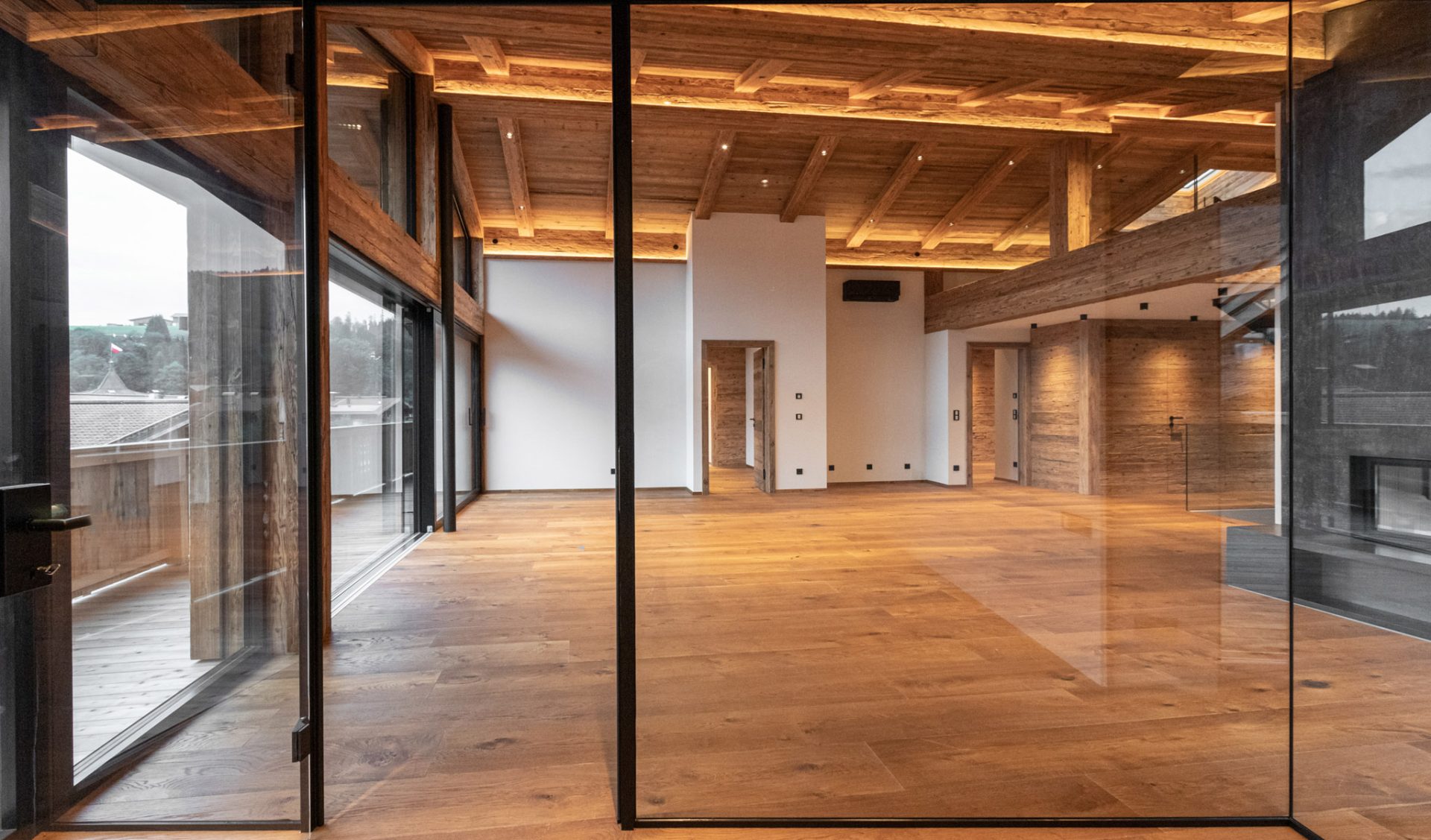 Luxus-Chalet-Innenraum mit Altholz-Kassettendecke, Natursteinwand, Glasfront und Massivholzparkett.