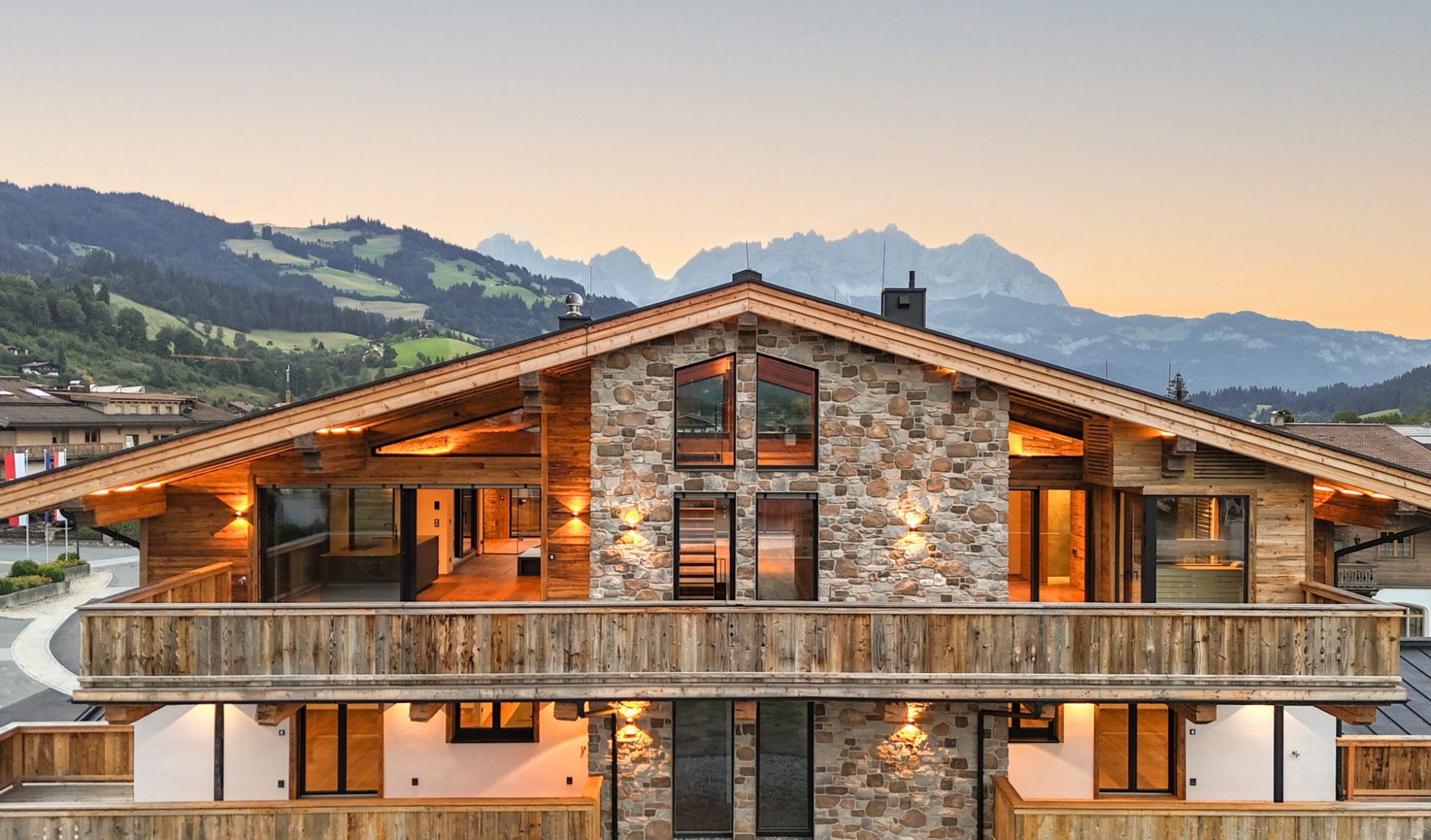 Exklusives Luxus-Penthouse mit Natursteinfassade, Altholzbalkon und Wilder Kaiser Panorama im Abendlicht.