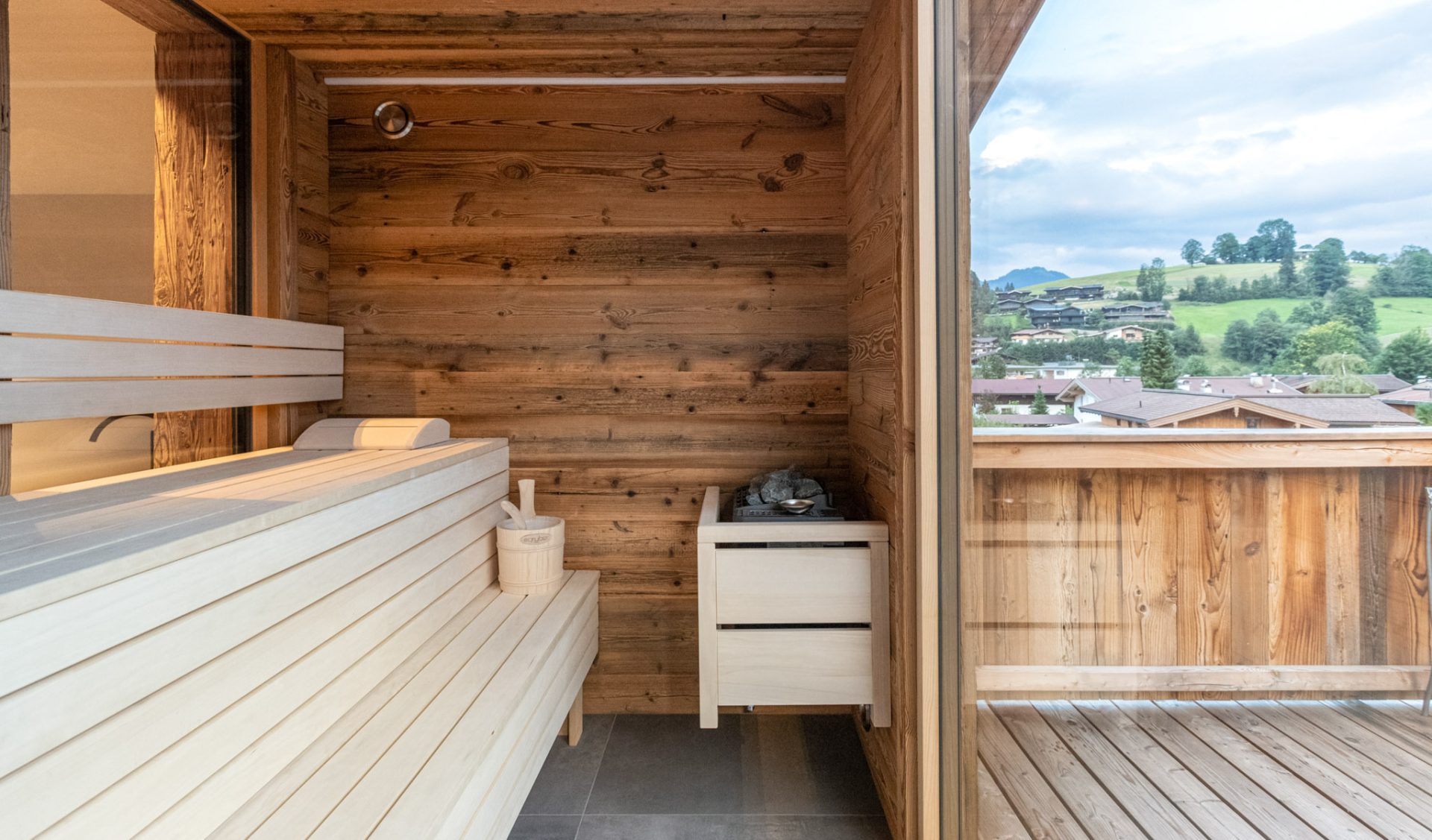 Private Außensauna mit Panoramablick auf Alpendorf und Bergwiesen auf überdachter Terrasse.