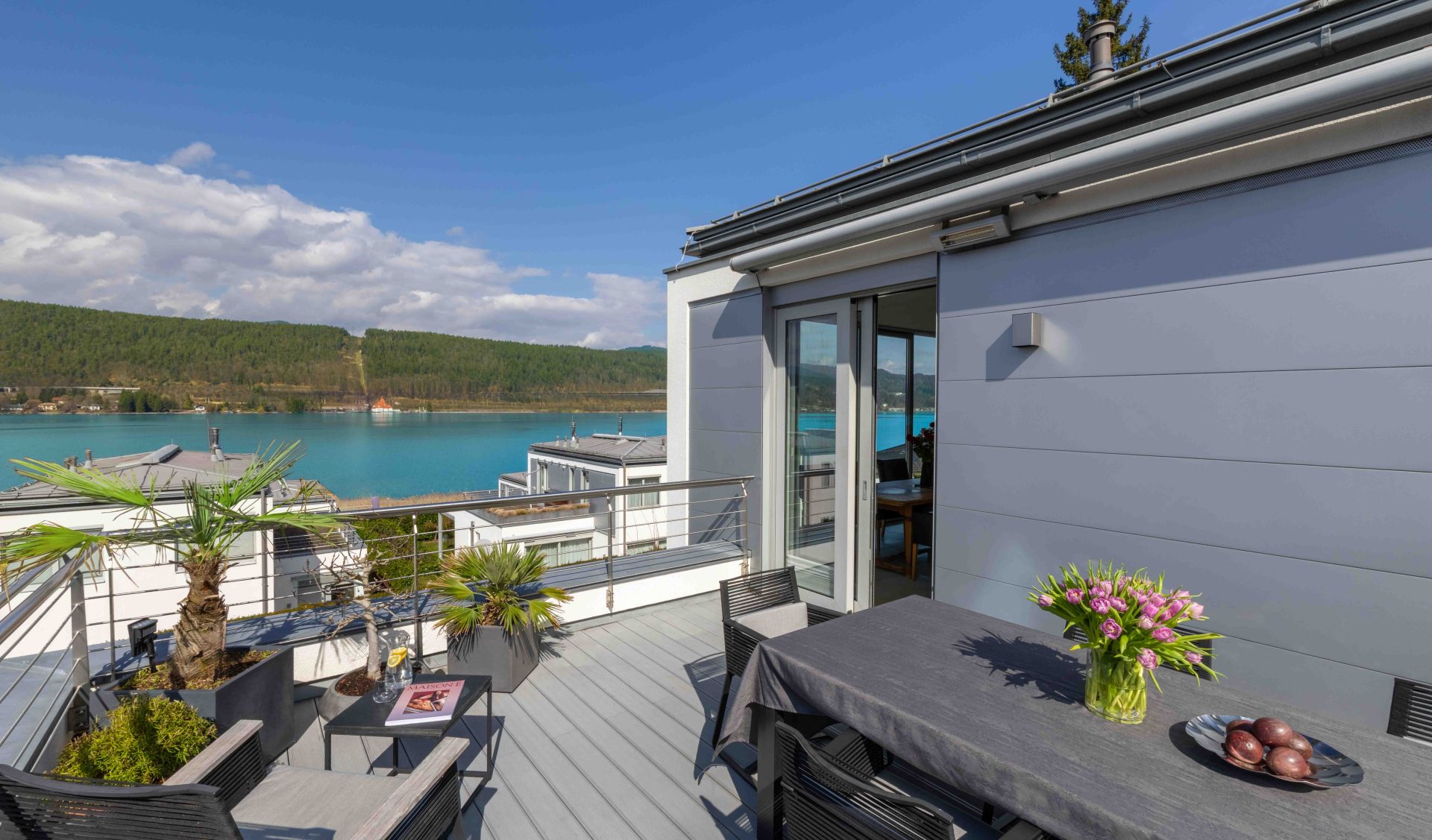 Große Dachterrasse des Penthouses mit modernem Esstisch, Lounge-Möbeln und Panoramablick auf den türkisfarbenen Wörthersee.