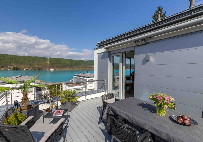 Große Dachterrasse des Penthouses mit modernem Esstisch, Lounge-Möbeln und Panoramablick auf den türkisfarbenen Wörthersee.