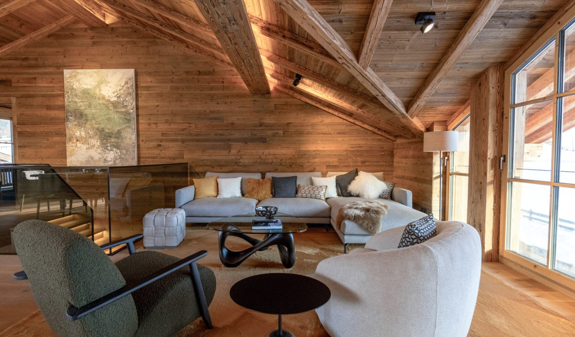 Offener Wohnbereich eines Luxus-Penthouses mit Altholz-Sichtdachstuhl und Panoramafenstern.