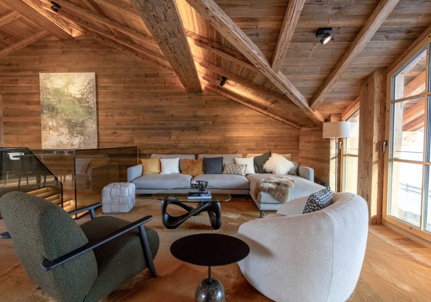 Offener Wohnbereich eines Luxus-Penthouses mit Altholz-Sichtdachstuhl und Panoramafenstern.