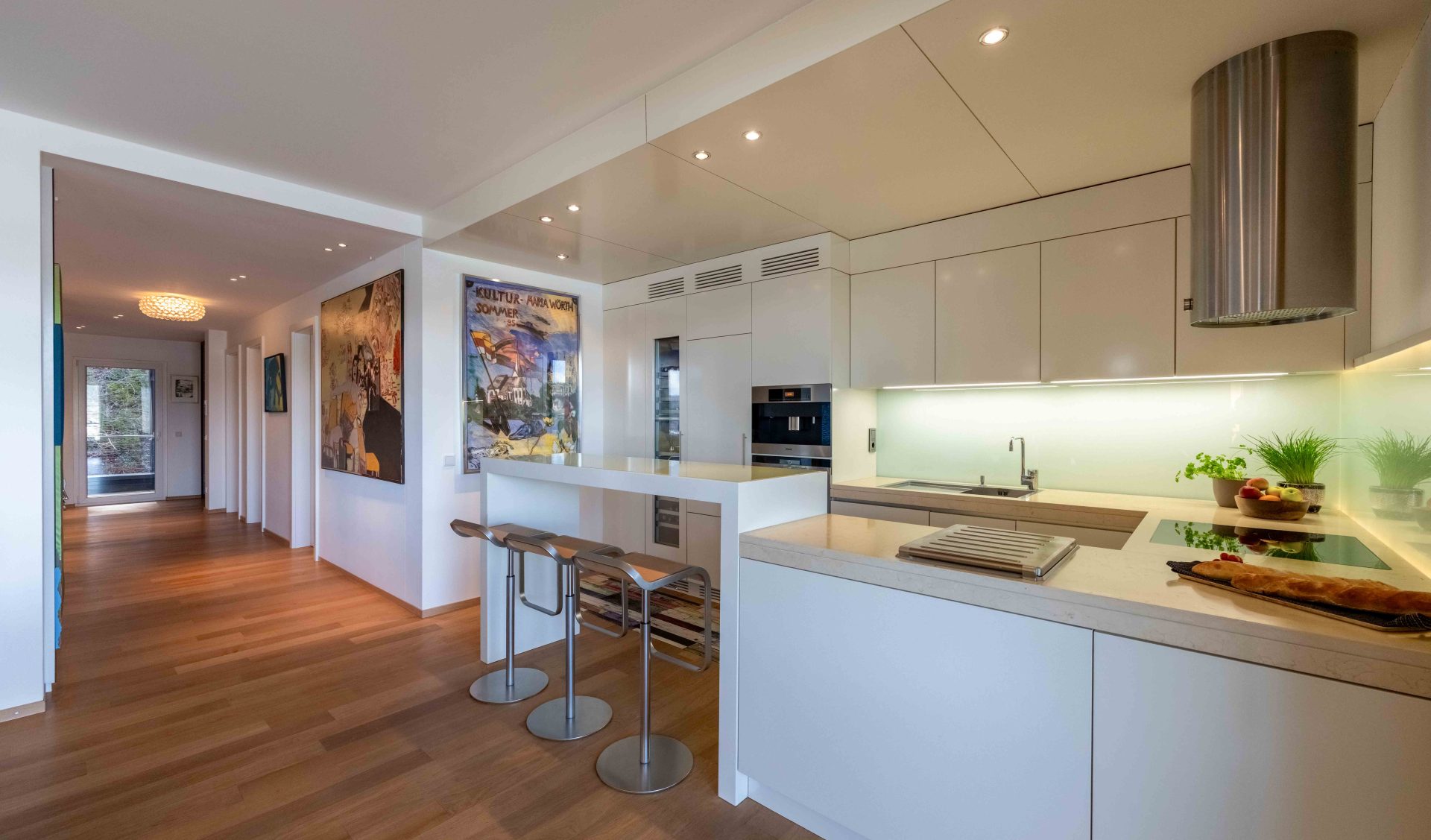 Moderne, helle Einbauküche mit Frühstücksbar und Barhockern, edlem Echtholzparkett und minimalistischem Design.