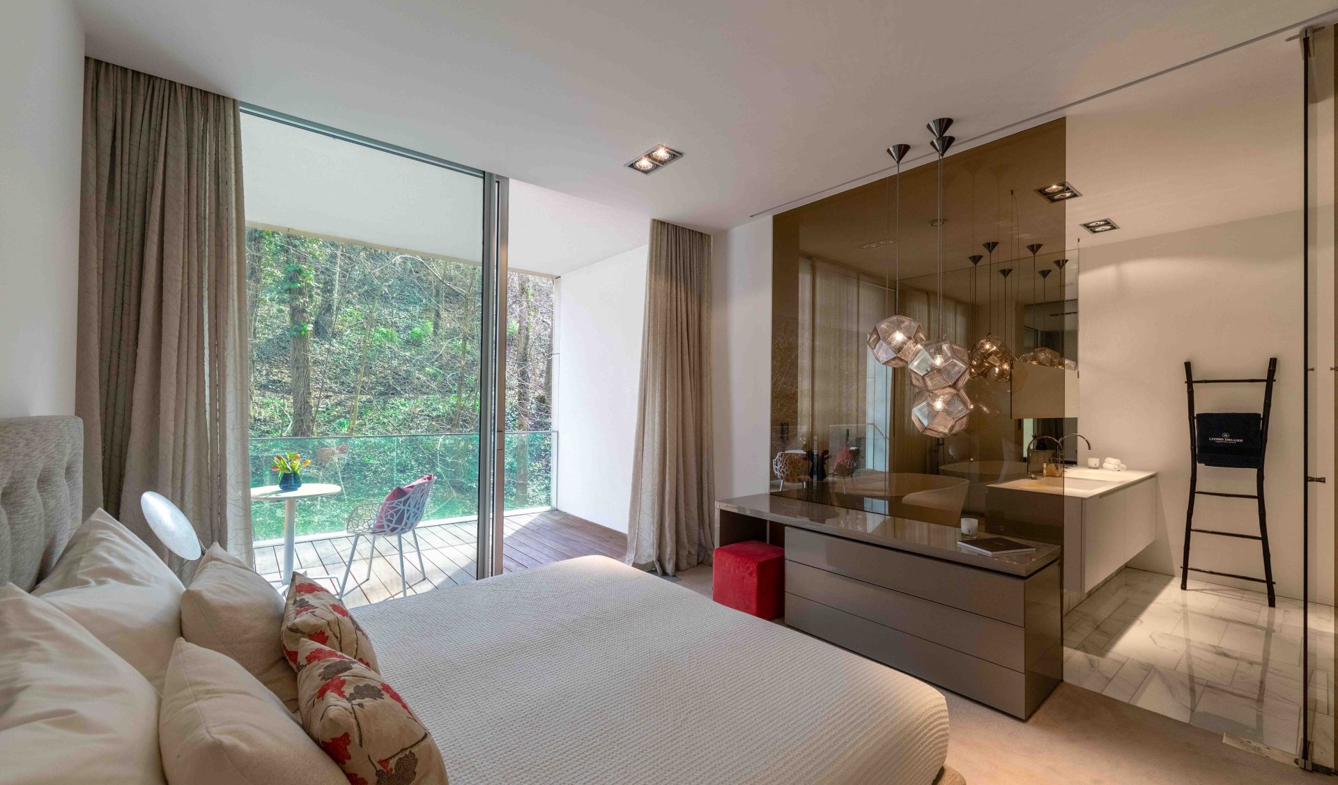 Elegantes Schlafzimmer mit direktem Zugang zum Balkon und Blick ins Grüne sowie angrenzendem, offen gestalteten Badezimmer.
