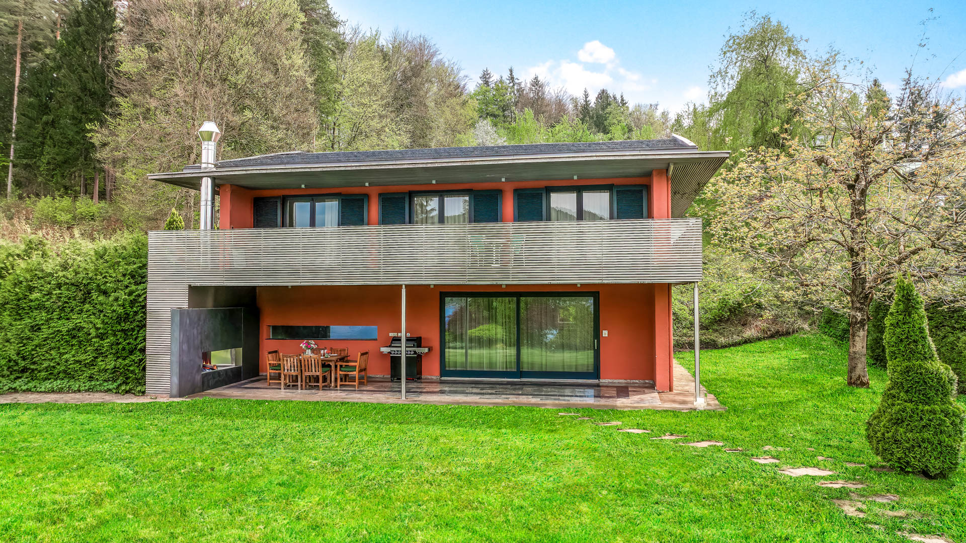 Außenansicht des zweigeschossigen Seehauses mit Terrasse und großzügigem Garten.