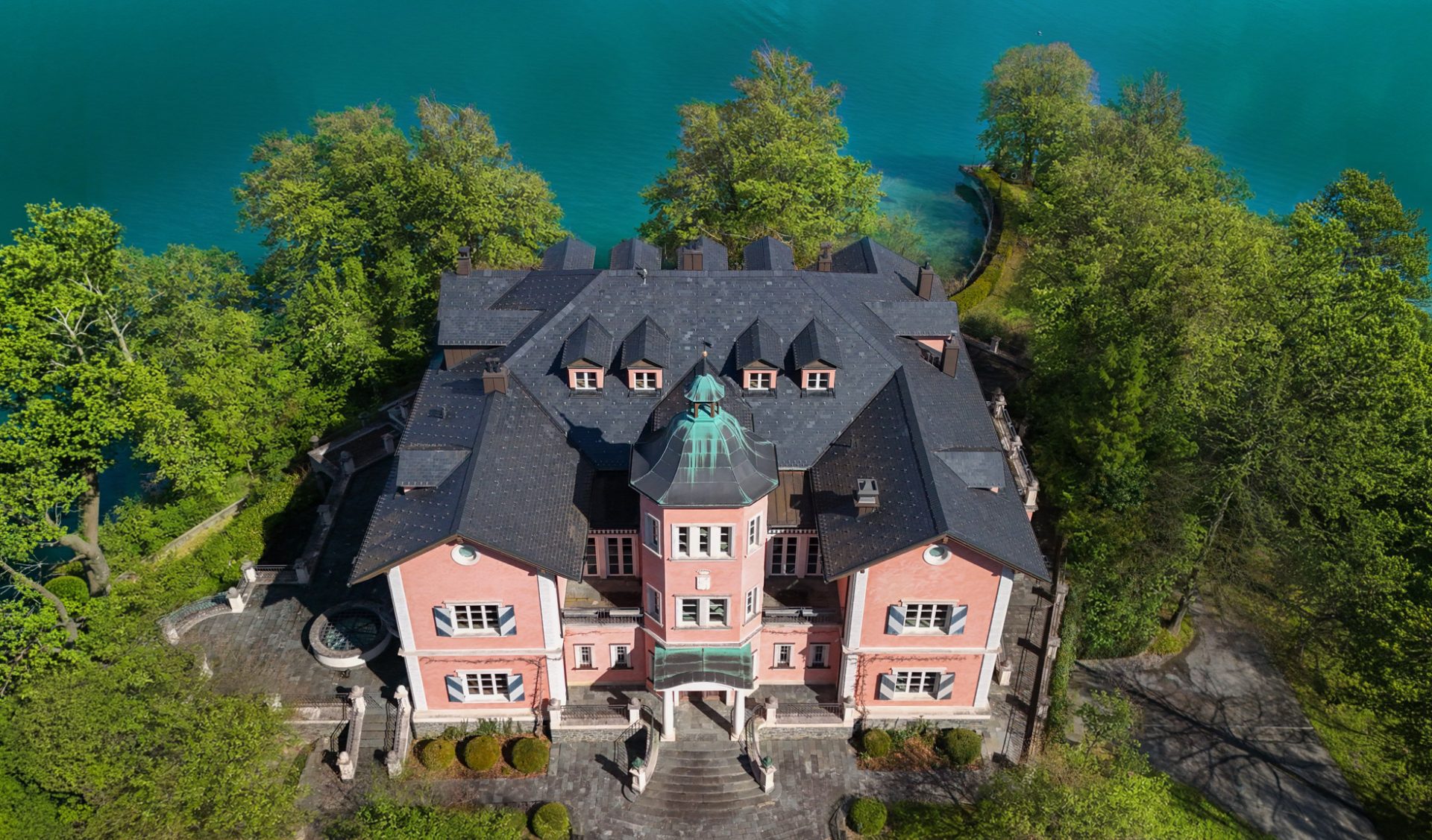 Historische Seevilla „The Grand" mit Kupferturm, umgeben von parkartiger Naturlandschaft am Wörthersee.