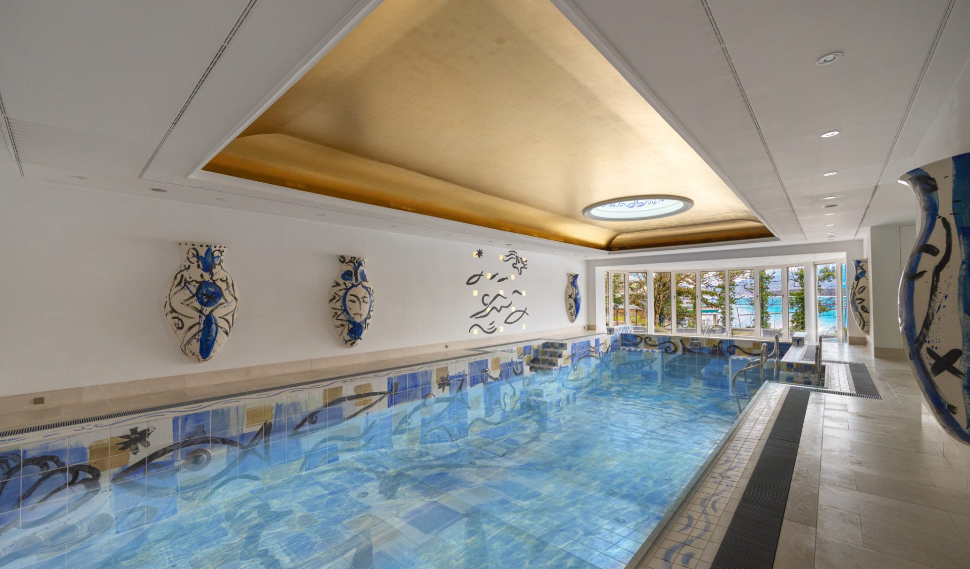Privater Indoor-Pool mit blauem Mosaikdesign und künstlerischer Wandgestaltung.
