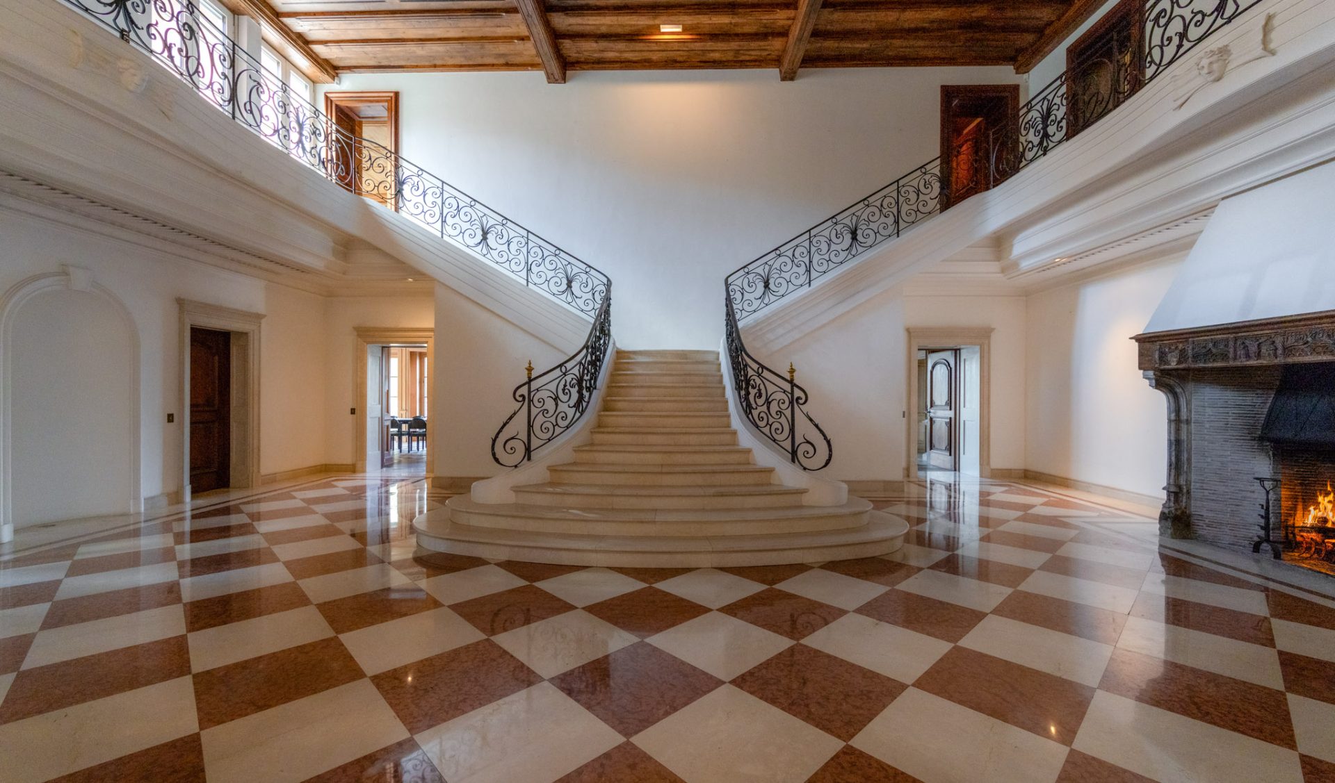 Großzügiges Entrée mit geschwungener Marmortreppe, Schmiedeeisengitter und offenem Kamin.
