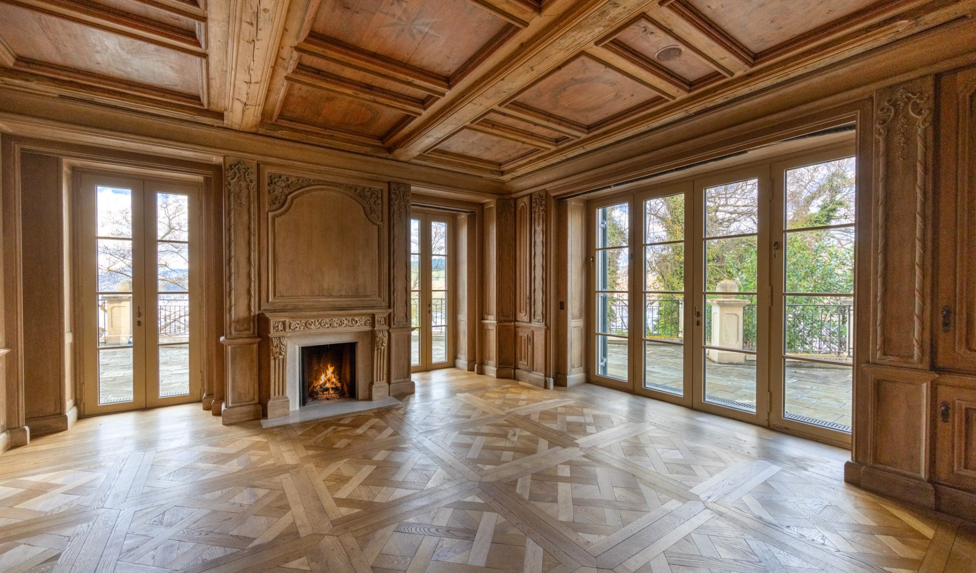 Historischer Salon mit kunstvoller Holzdecke, Wandvertäfelung und offenem Kamin.