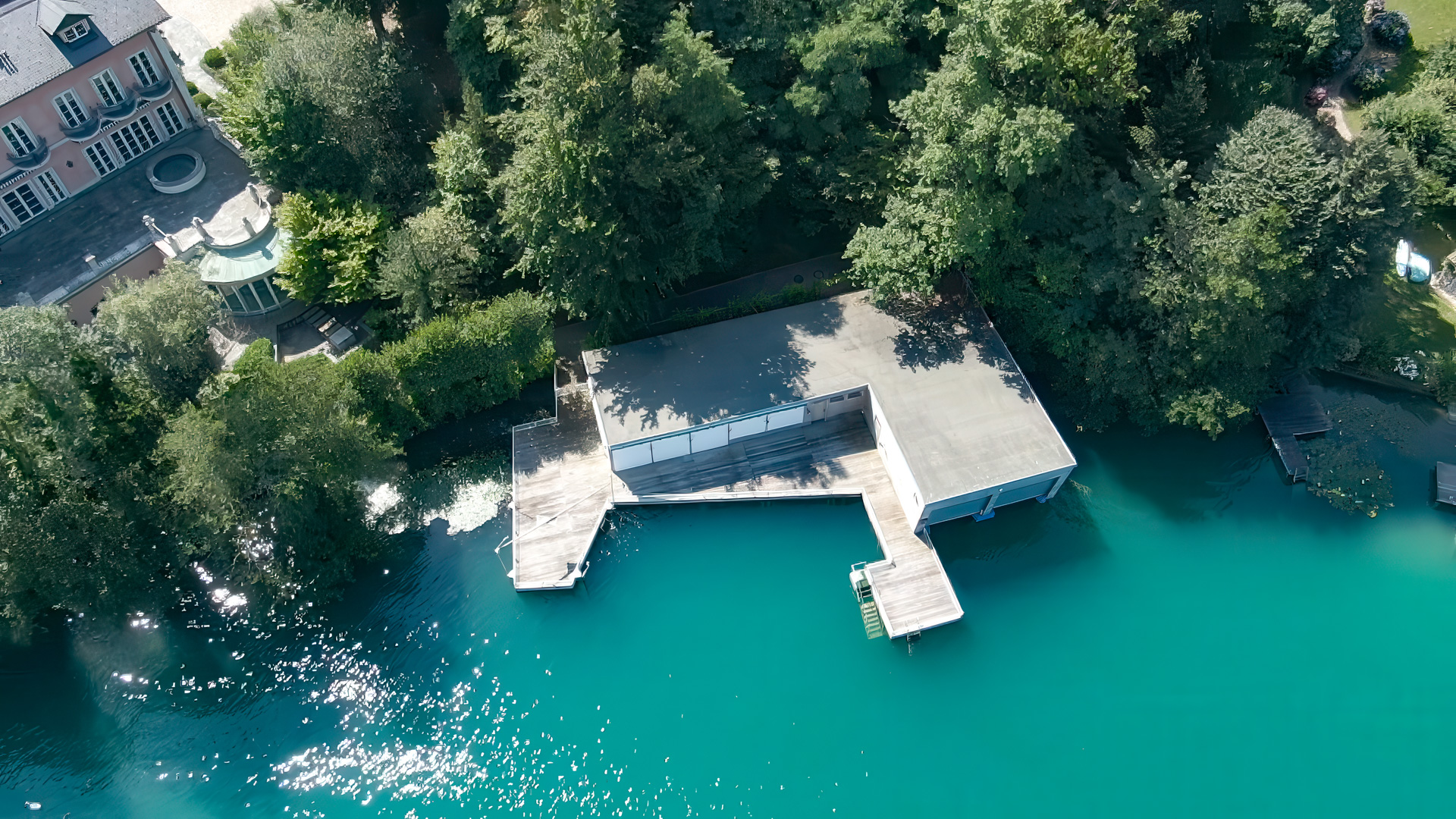 Luftaufnahme des großzügigen Bootshauses mit Badeplattform und Steg am türkisfarbenen Wörthersee.